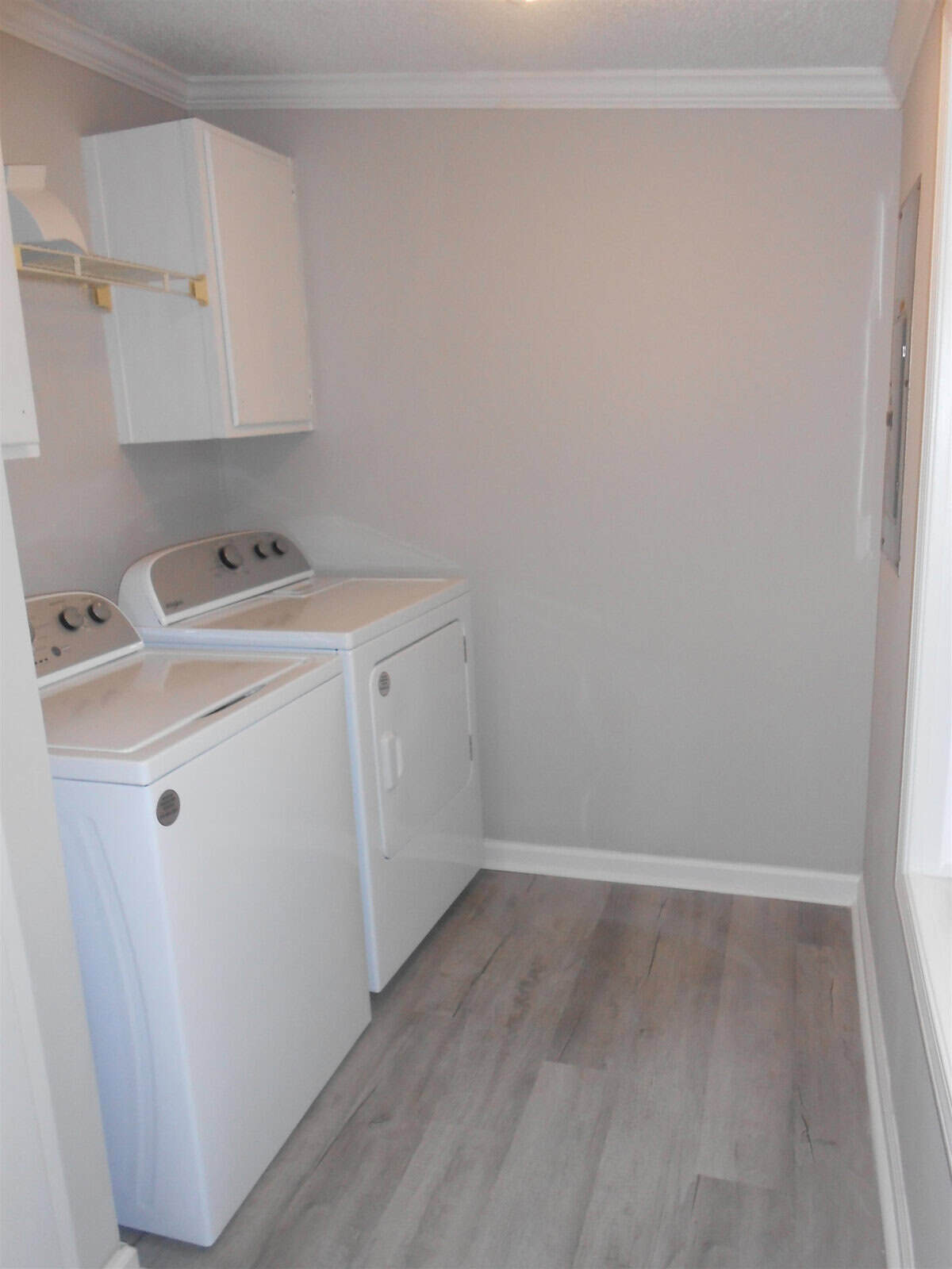 A small, clean laundry room with a white washer and dryer, white cabinets, and light grey flooring.