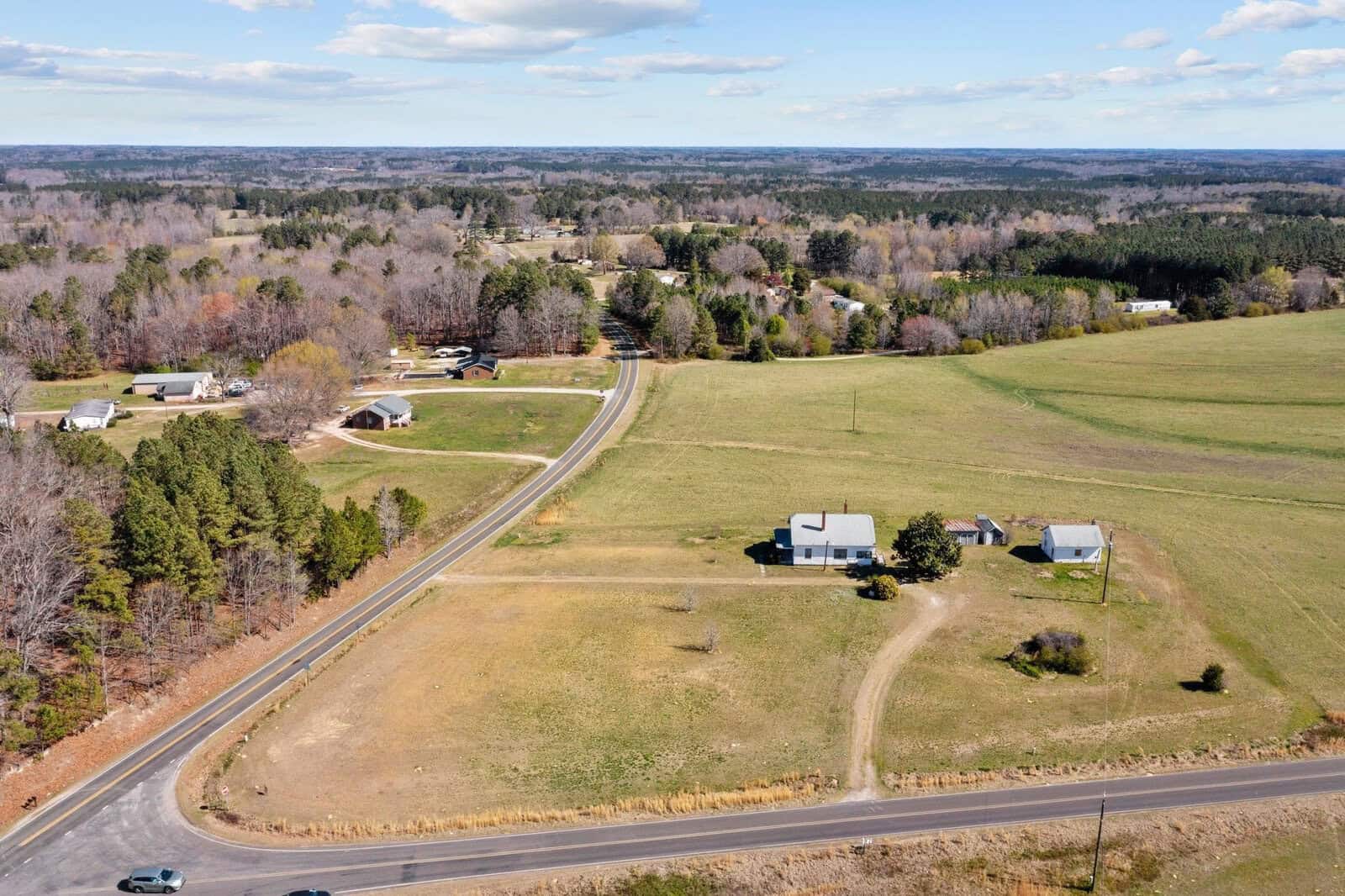 Aerial view of a rural landscape featuring a road, with scattered houses surrounded by fields and patches of trees.