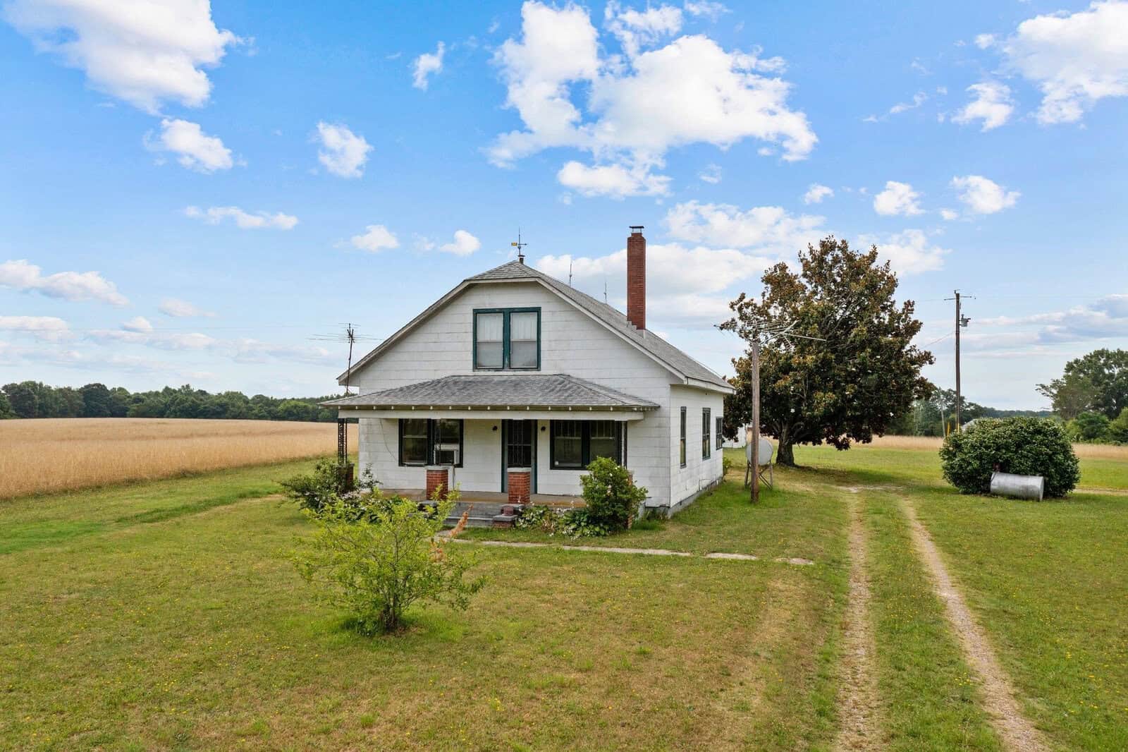 A small, white countryside house with a gabled roof and a chimney, set against a background of a clear sky and a vast, golden wheat field at 1558 Cheeks Quarter Road, Henderson