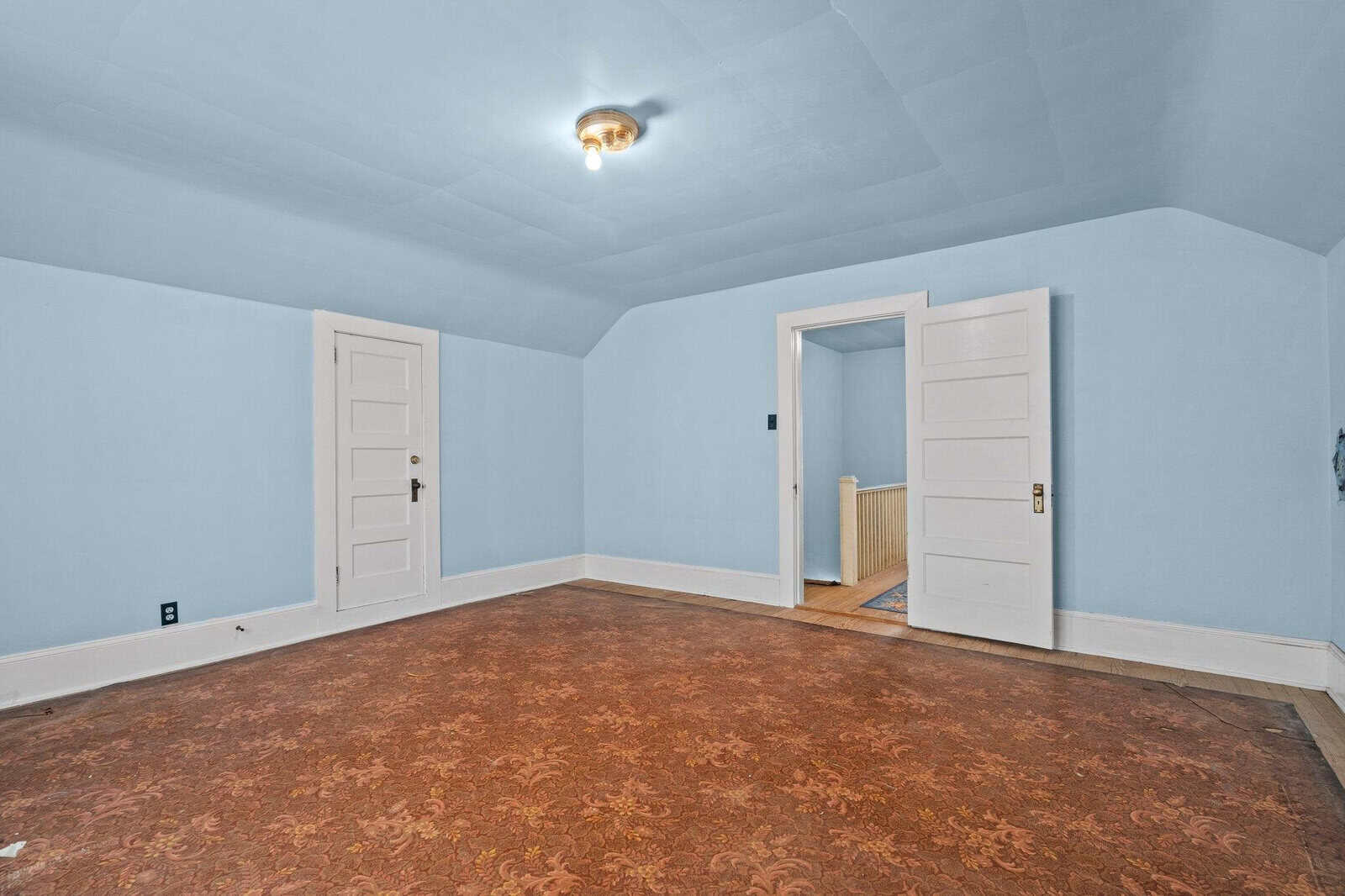 An empty room with light blue walls, two white doors, and a patterned brown carpet.