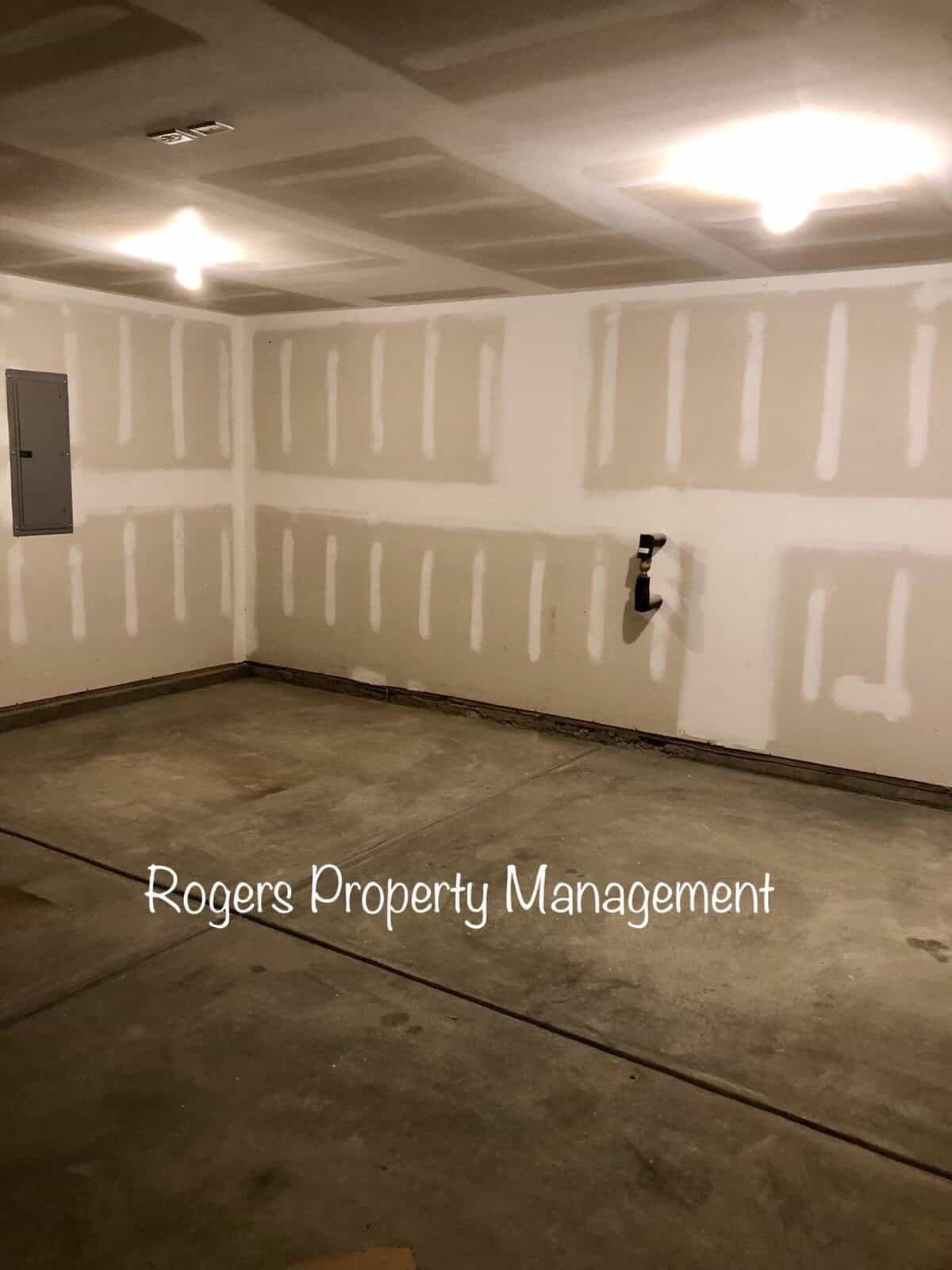 An empty garage with unfinished drywall and the text "rogers property management" superimposed on the image.