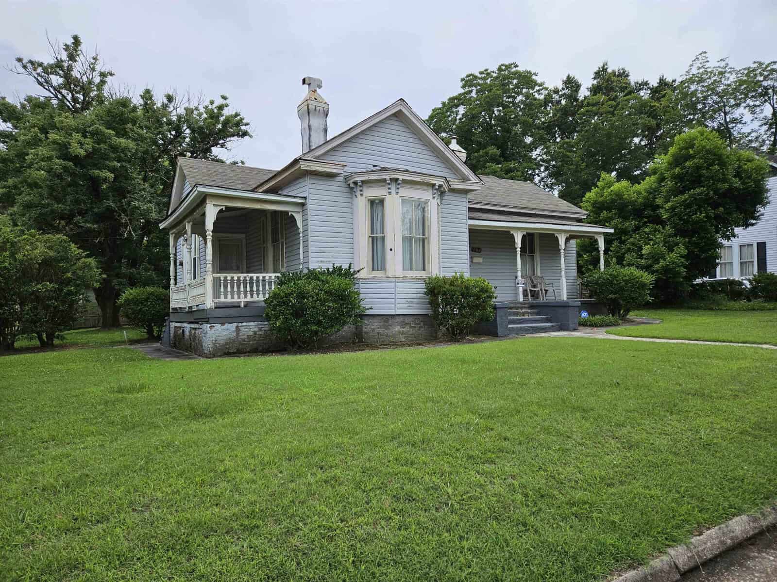 A single-story house with light blue siding and white trim, featuring a front porch and a green lawn.