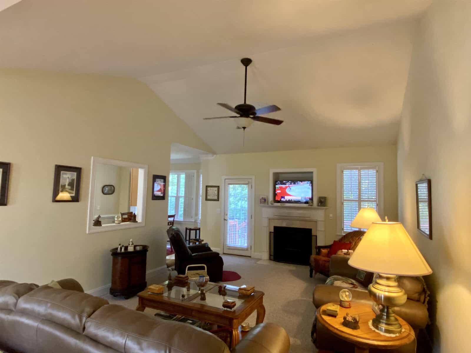 A well-lit living room featuring a ceiling fan, a fireplace, a mounted television, and comfortable seating arranged around a central coffee table.