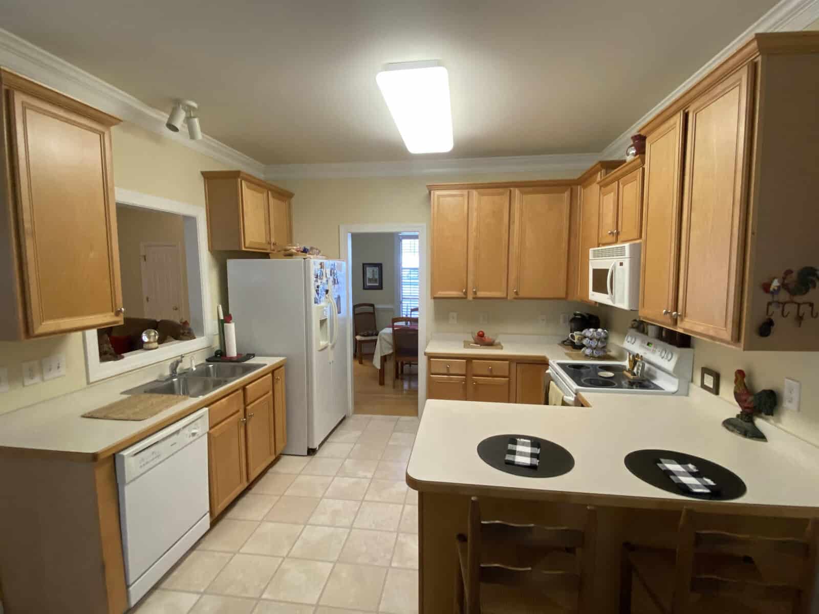 A well-lit, spacious kitchen with wooden cabinets, white appliances, and a central island with two black stools.