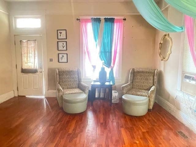 A cozy sitting corner with two patterned upholstered chairs facing a window adorned with pink and blue translucent curtains, situated in a room with hardwood floors and decorative items on the walls.