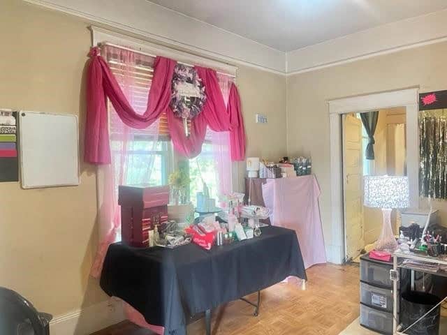 An indoor room with pink curtains, a table with various items, and multiple shelves containing assorted products.