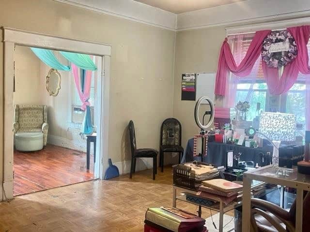A room with a hardwood floor, decorated with contrasting color curtains and various pieces of furniture, including chairs, a mirror, and a table with items scattered on it.
