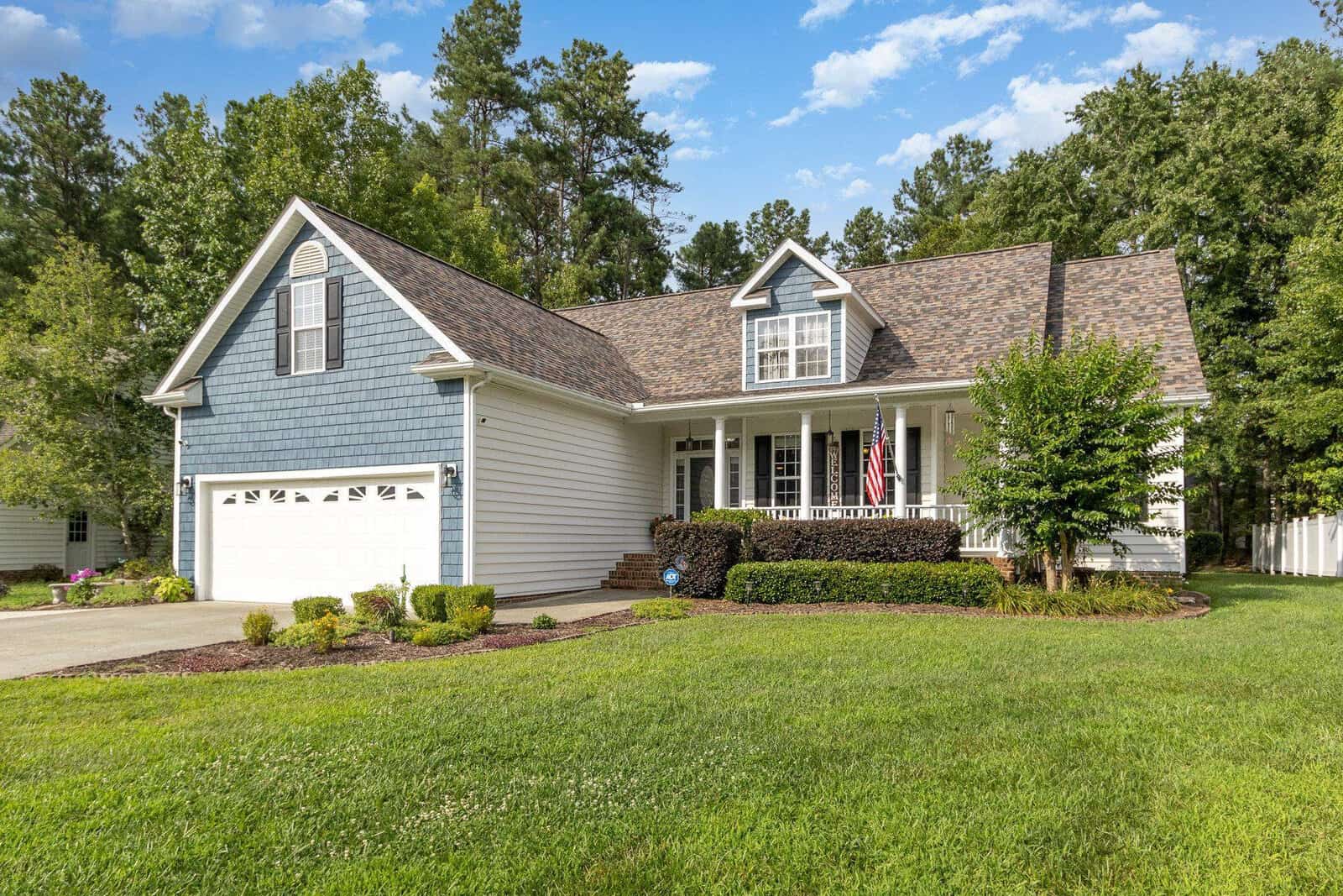 A single-family home with blue siding, a two-car garage, and a well-manicured lawn under a clear sky.