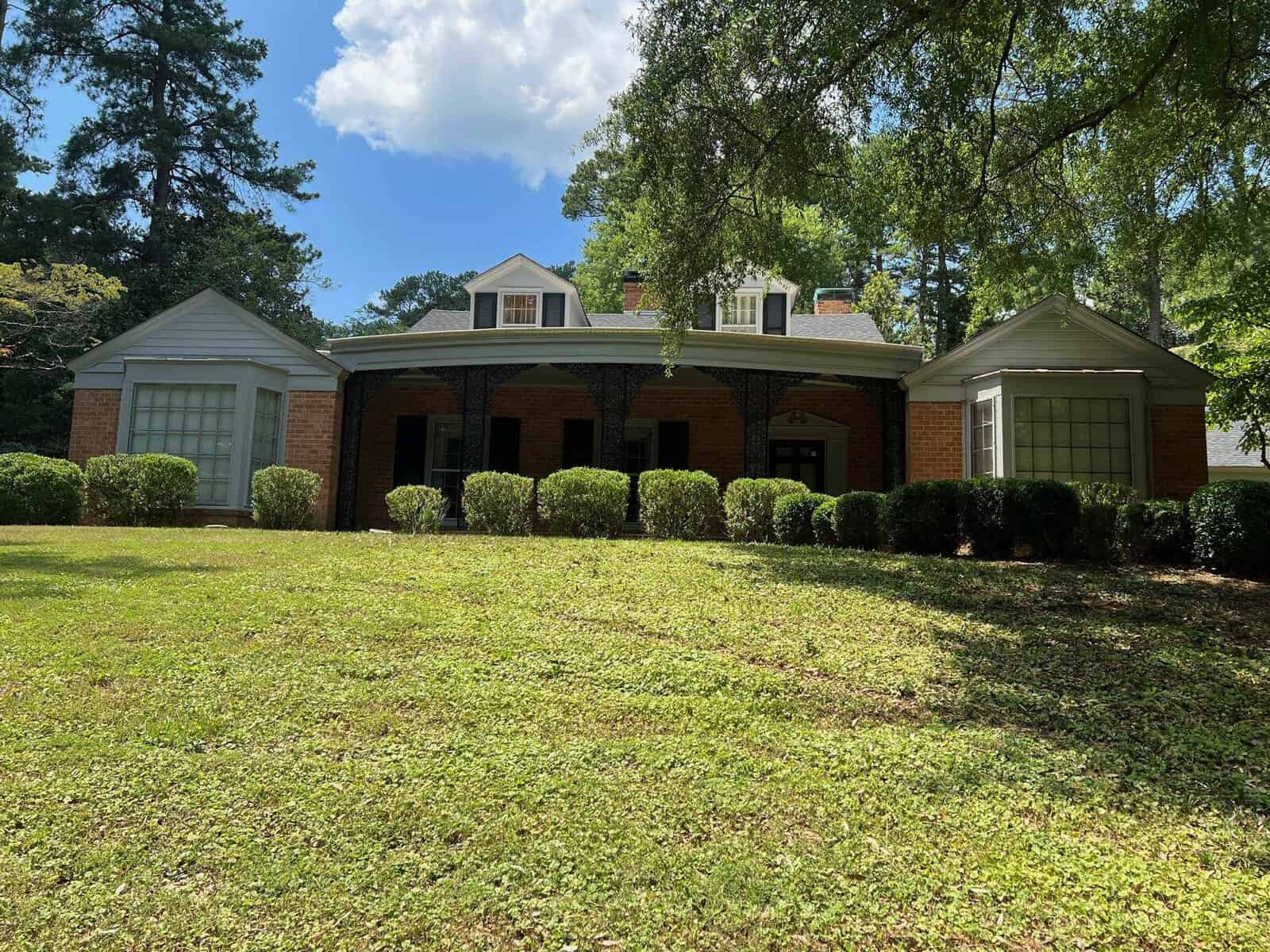 A single-story brick house with white trim and a large front lawn on a sunny day.