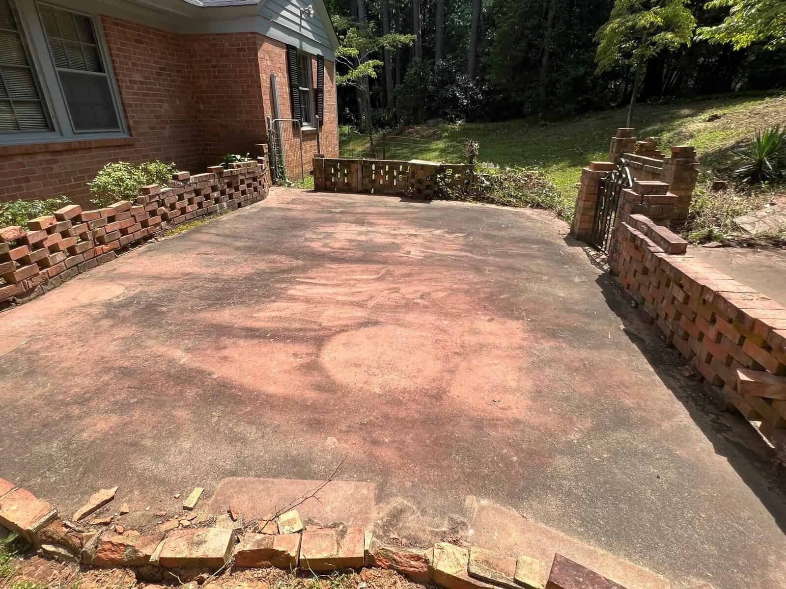 A weathered concrete driveway flanked by a damaged brick wall, leading up to a residential building.