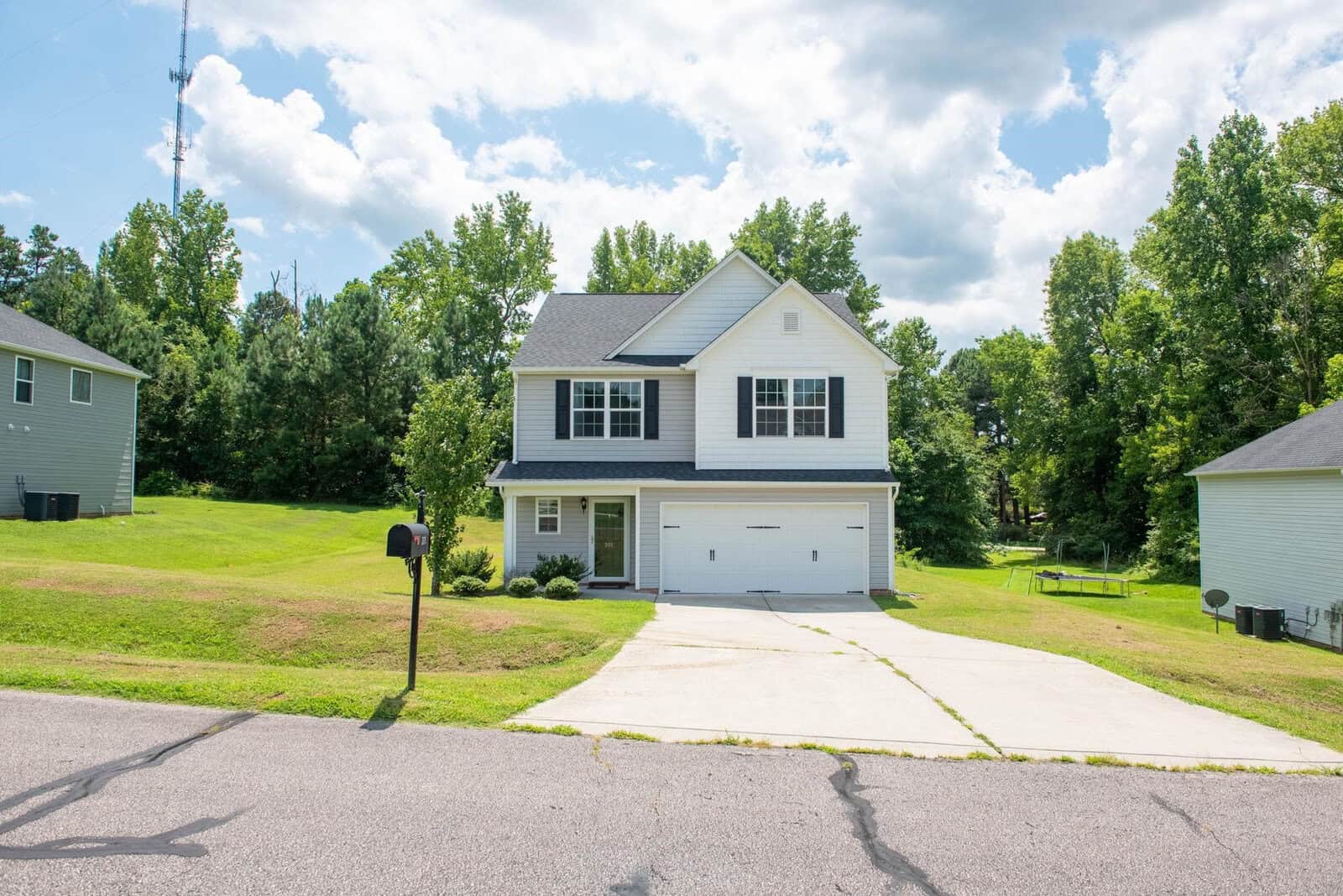 A two-story suburban home with a two-car garage and a front lawn, located on a sunny day with clear skies.
