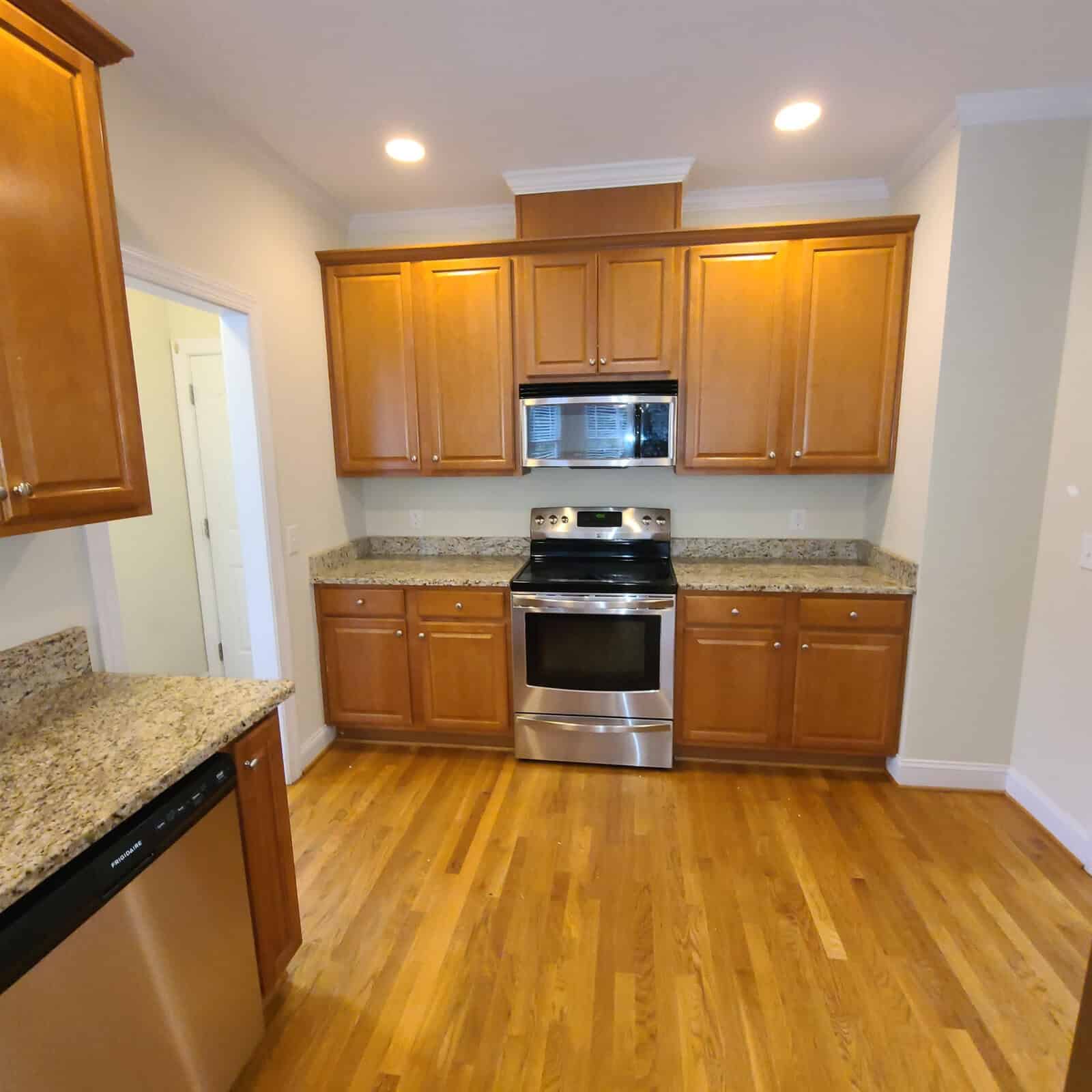 A modern kitchen featuring stainless steel appliances, granite countertops, and wooden cabinetry with a hardwood floor.
