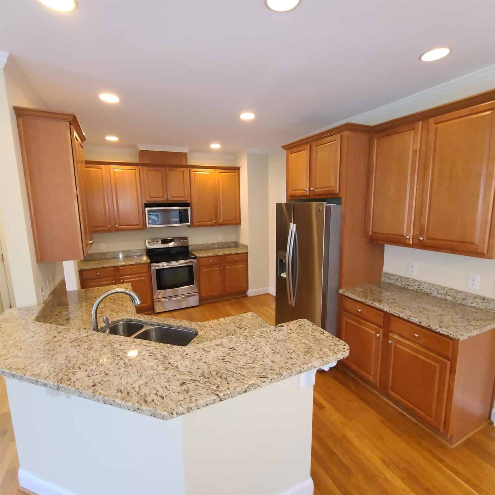 A well-lit kitchen featuring wooden cabinets, stainless steel appliances, granite countertops, and a central island.