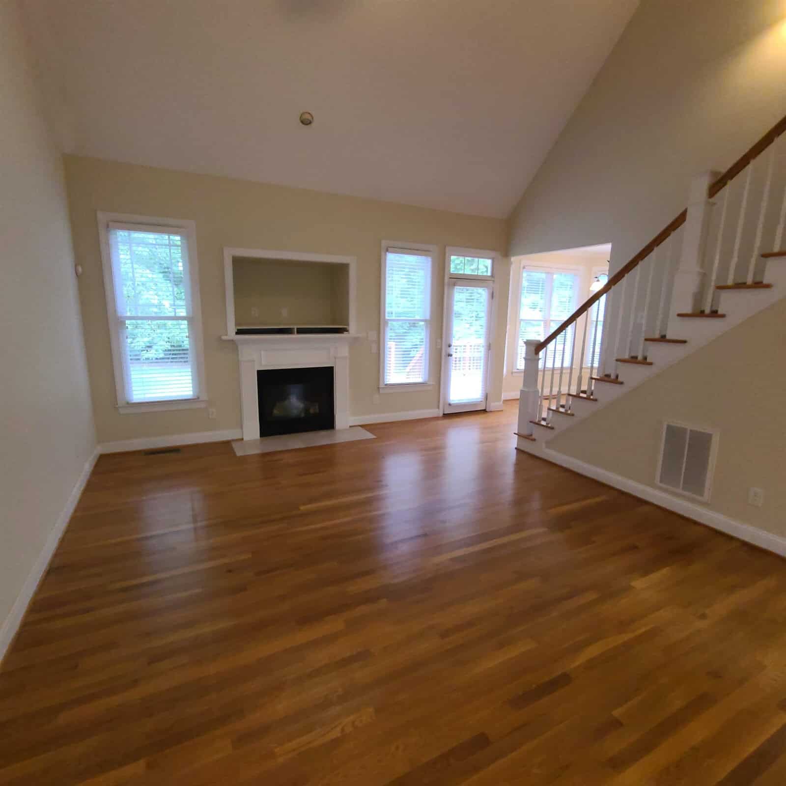 A vacant living room with hardwood floors, a fireplace, and staircase leading to the upper level.