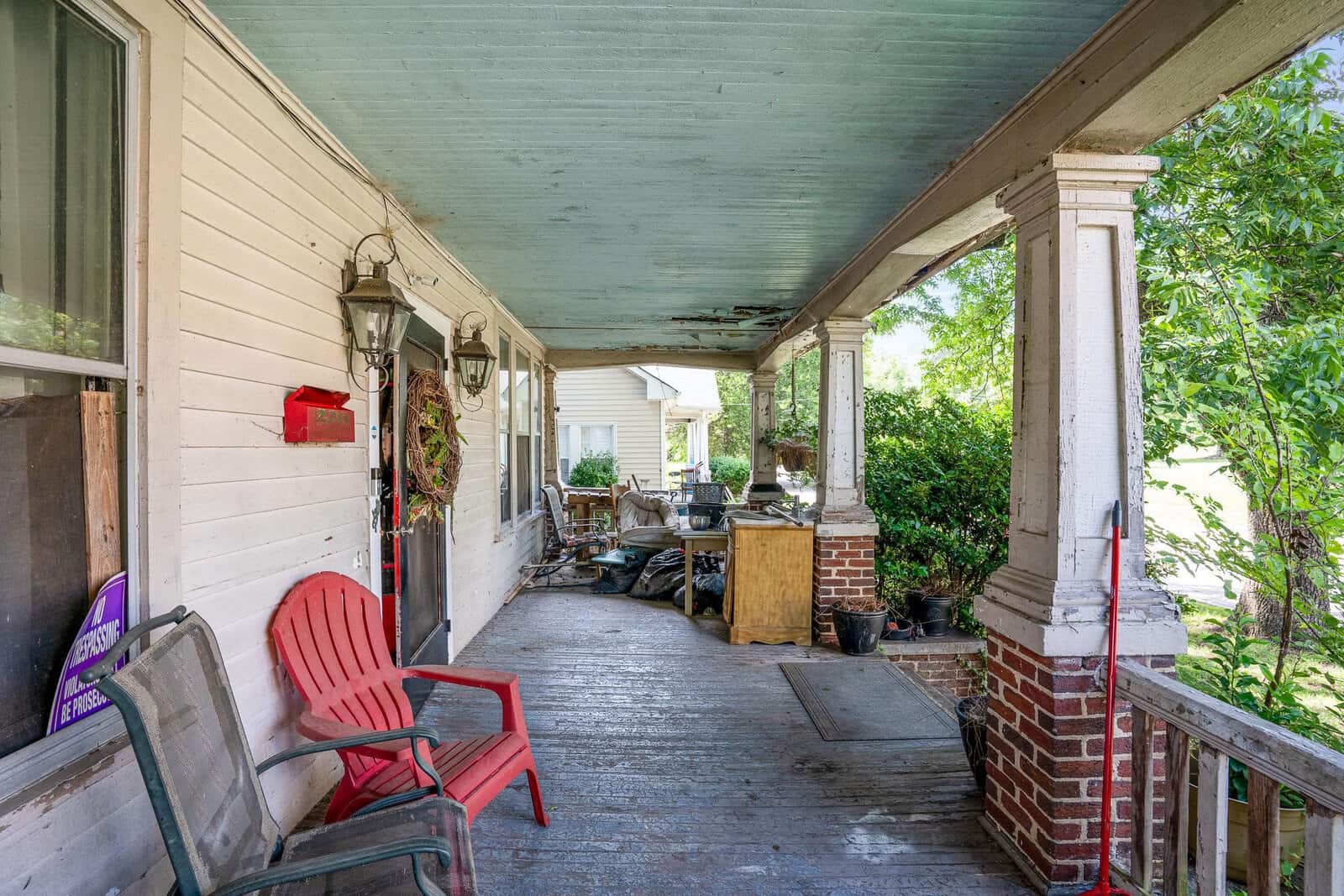 A cluttered residential porch with a red chair on the left, various items scattered throughout, and a green ceiling.