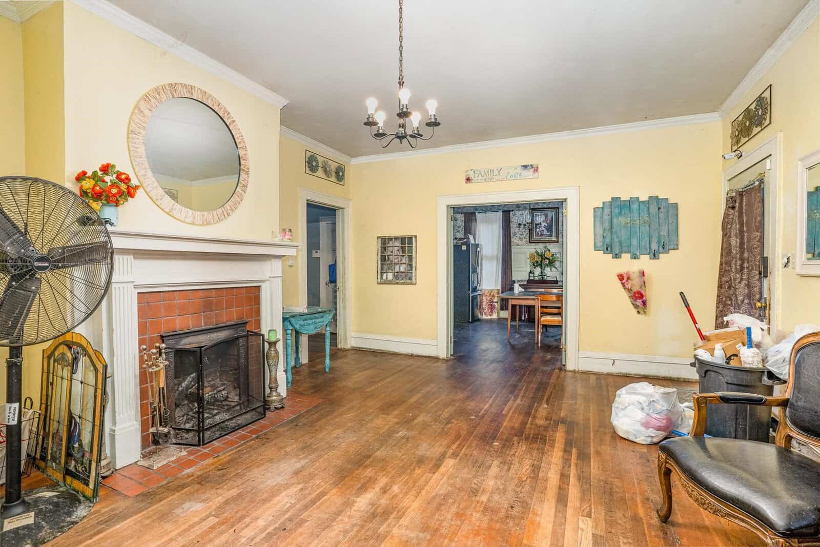 Interior of a vintage-styled living room with a fireplace, wooden floors, and assorted furnishings and decorations, showing signs of everyday use.