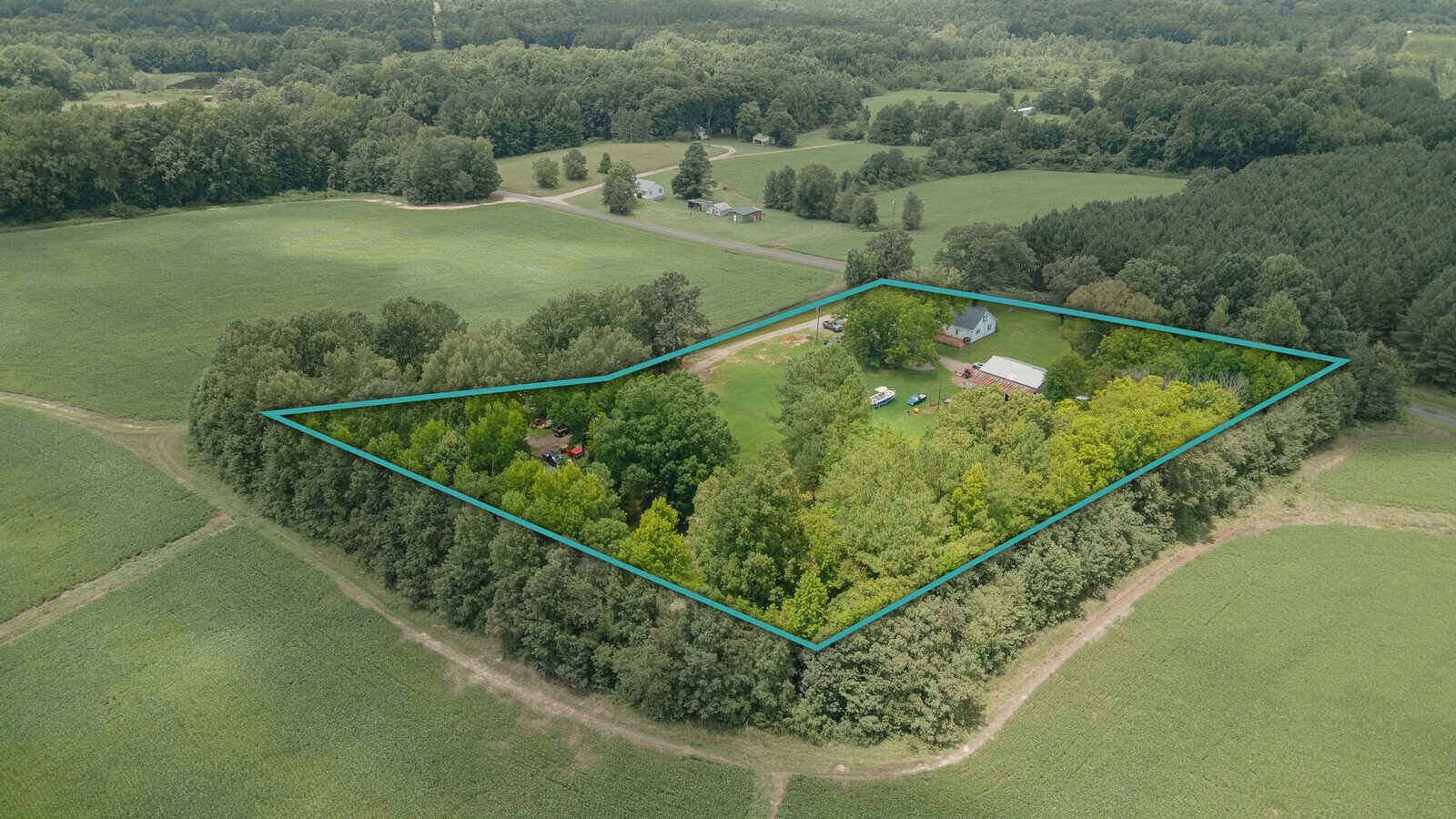 An aerial view of a rural property outlined in blue, featuring a cluster of buildings amid a landscape of fields and trees.