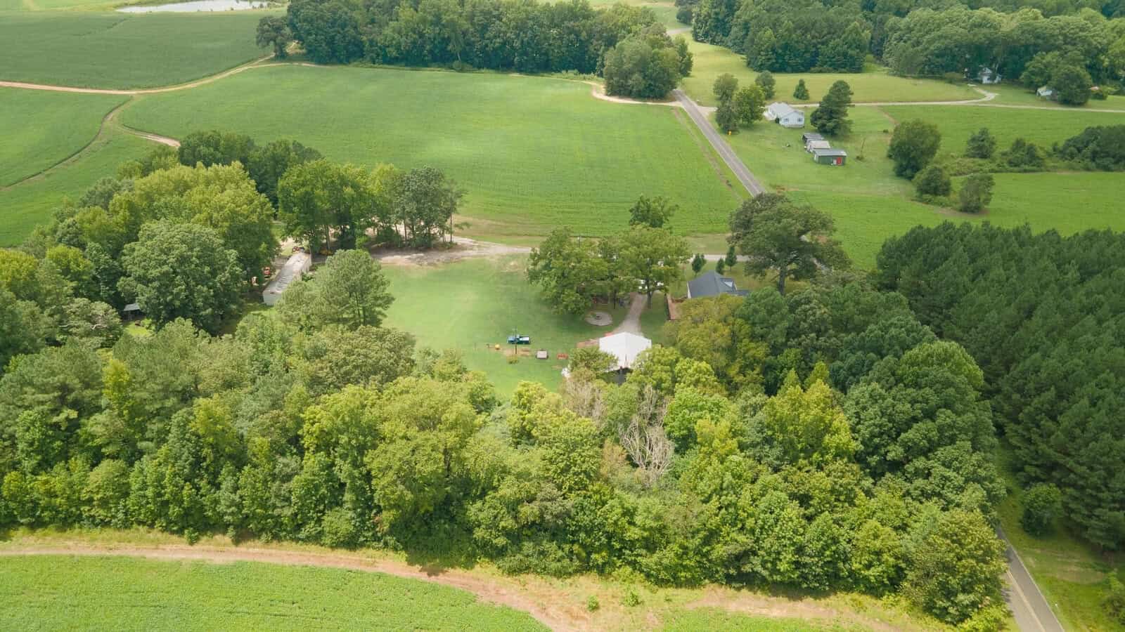 Aerial view of a rural landscape showing fields, a road, and houses surrounded by greenery.