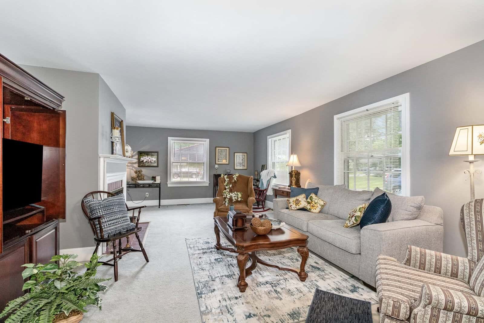 A neatly arranged living room with gray walls, furnished with a sofa, armchairs, a coffee table, and decorative items, illuminated by natural light from two windows.