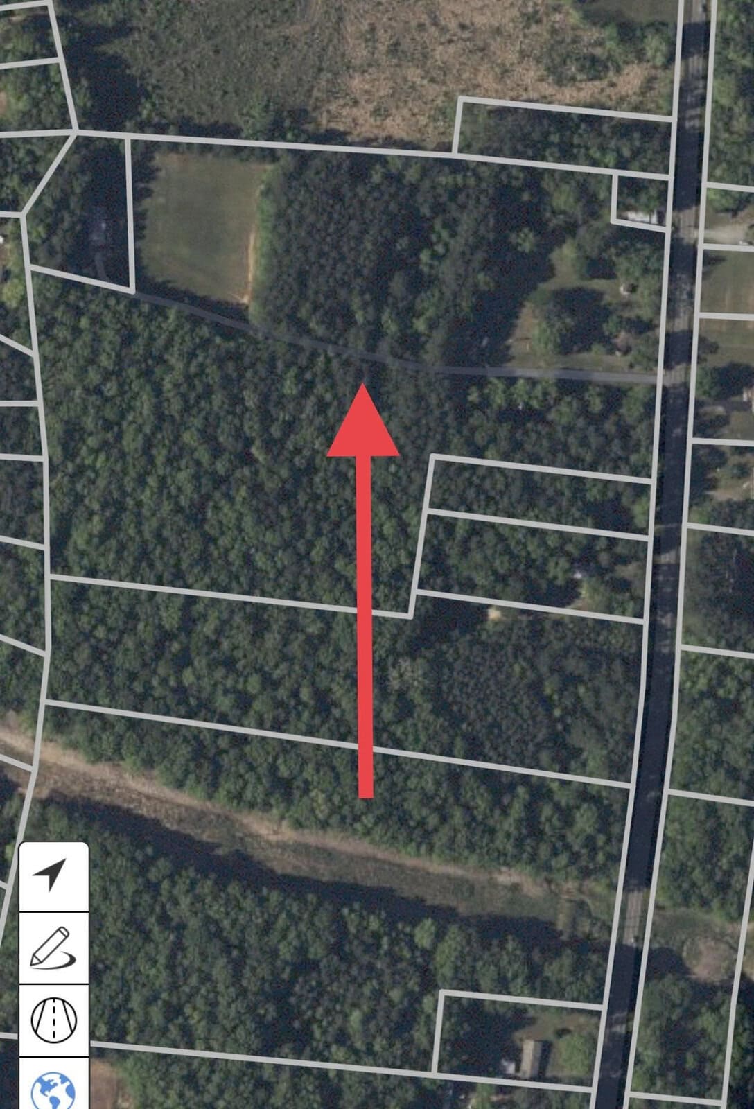 Aerial map view showing a red arrow pointing north over a forested area near Oxford. Several property boundary lines are visible alongside 7029 N NC 15 Highway, with a road on the right. Navigation symbols appear at the bottom left corner of the map.