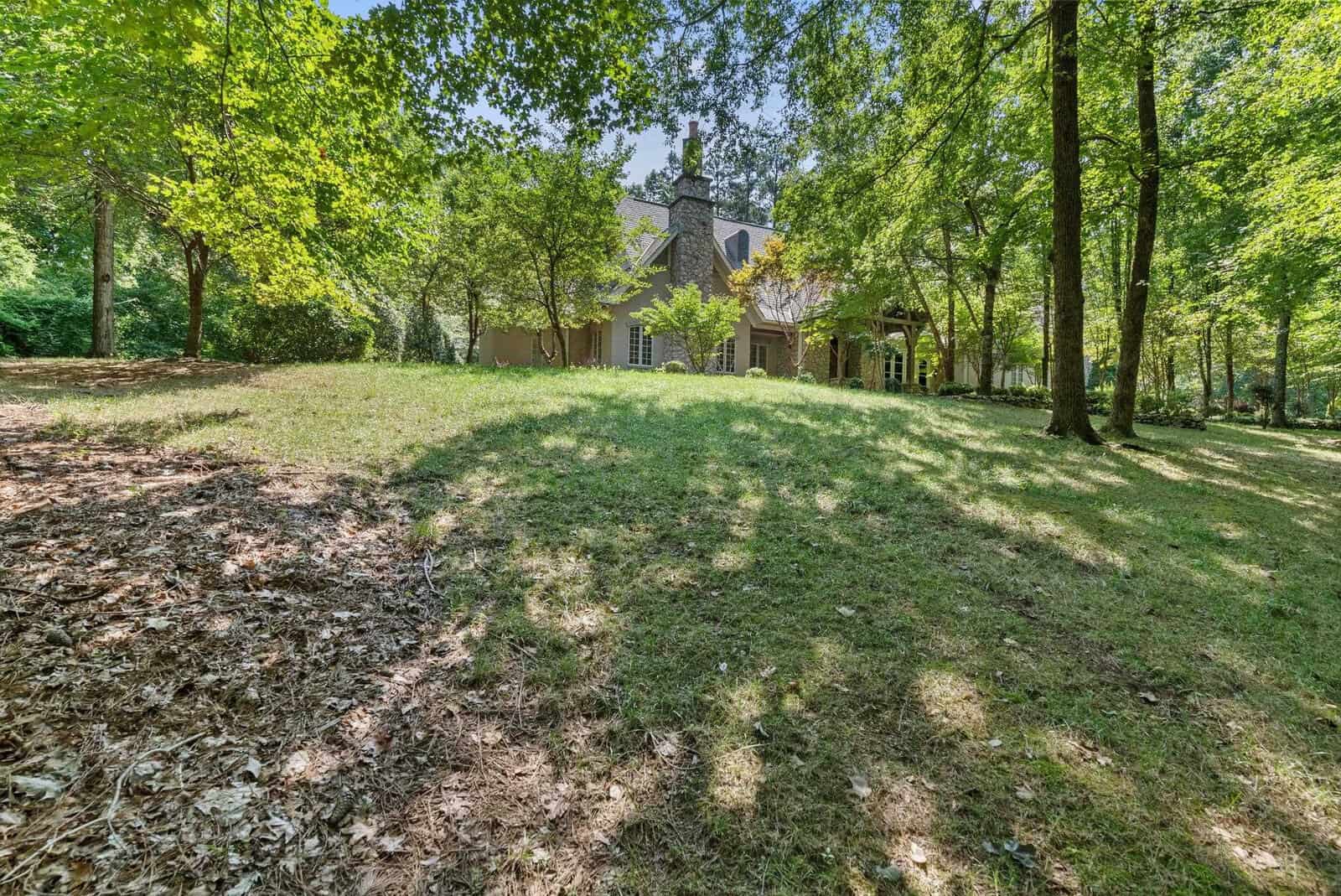 A spacious lawn leading up to a two-story house partially obscured by trees on a sunny day.