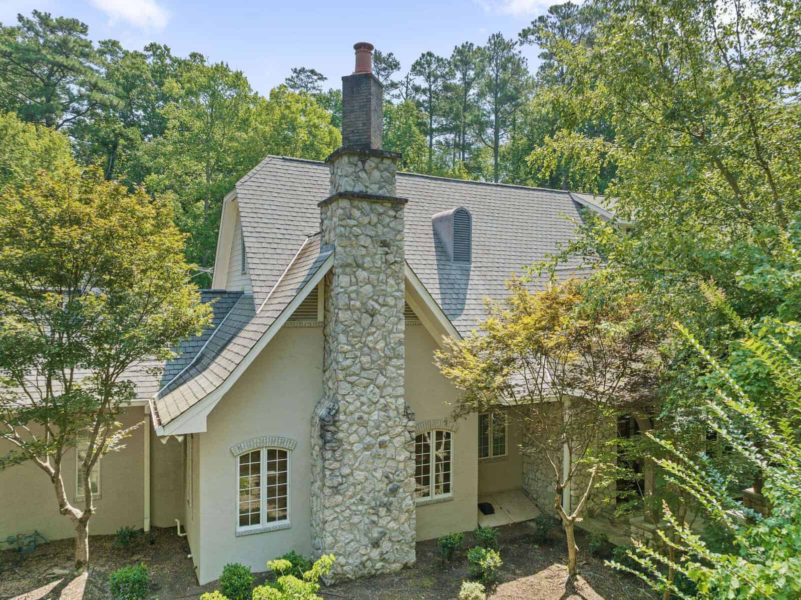 Aerial view of a two-story house with a large stone chimney, surrounded by green trees.