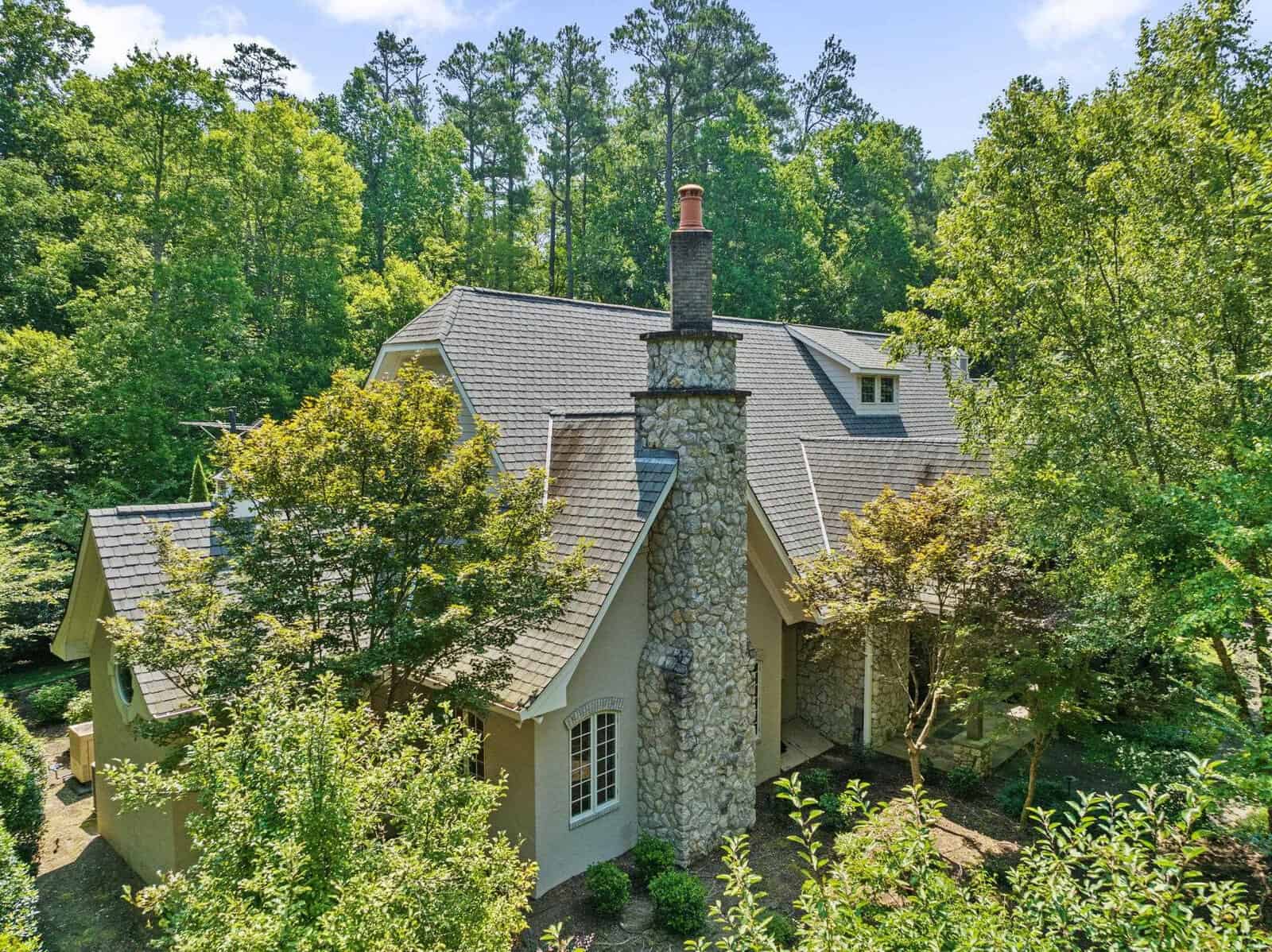 Aerial view of a stone chimney house with beige walls nestled amongst lush green trees.