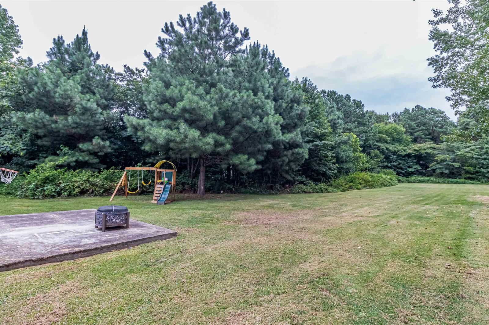 A quiet playground with a swing set beside a large, grassy area, surrounded by trees with overcast skies above.