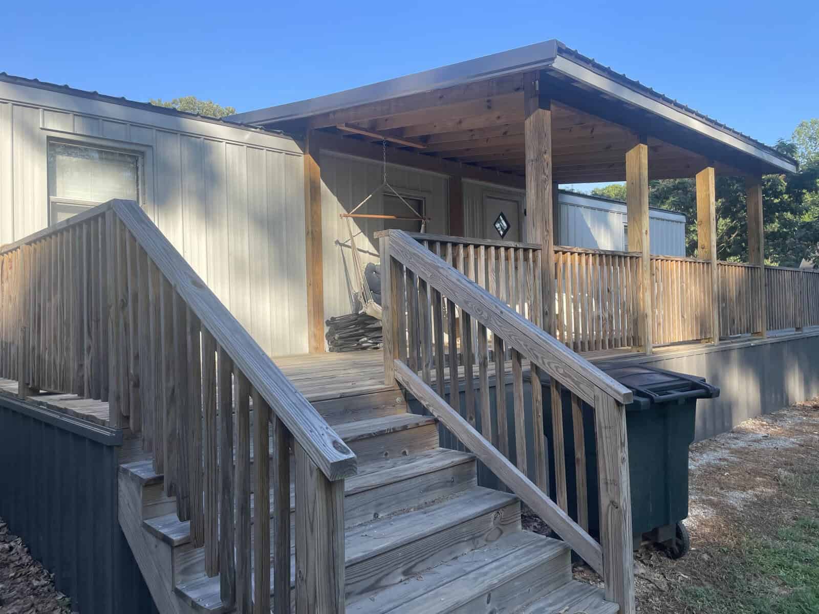 A wooden staircase leading up to the porch of a gray mobile home on a sunny day.