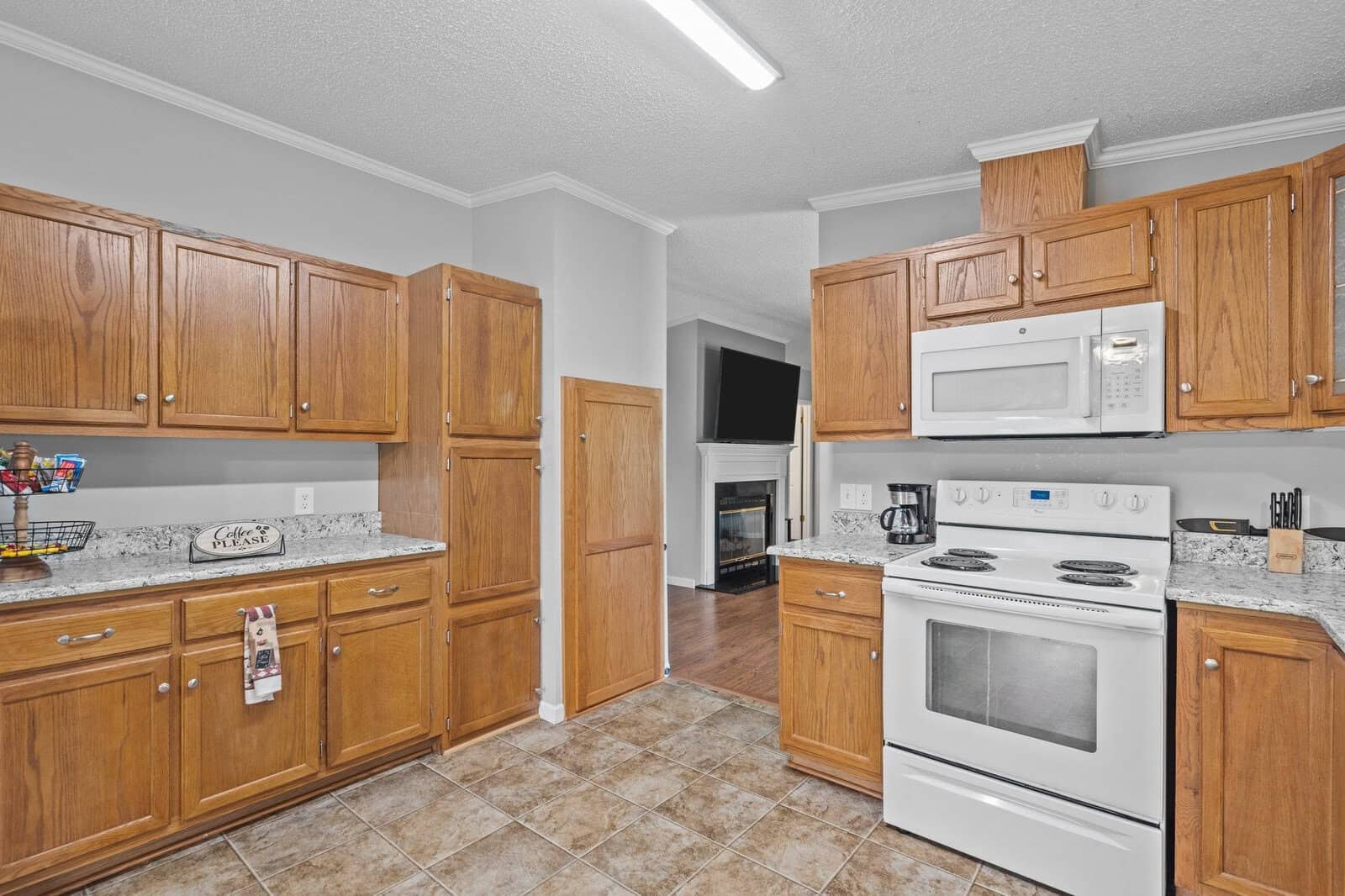 A modern kitchen with wooden cabinets, white appliances, and tiled flooring.