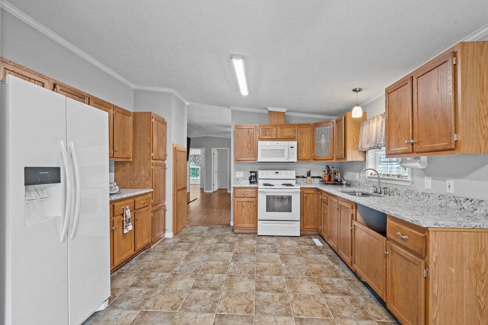 A spacious kitchen with wooden cabinetry, granite countertops, white appliances, and tiled flooring.