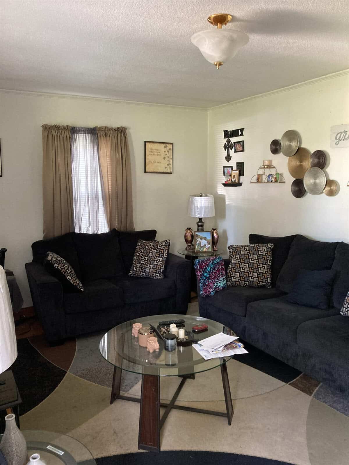 A cozy living room with two dark sofas, a glass coffee table, and decorative items on the walls.
