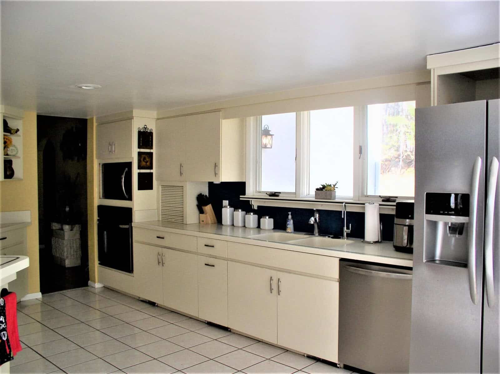 A well-lit kitchen with white cabinetry, stainless steel appliances, and a tile floor.