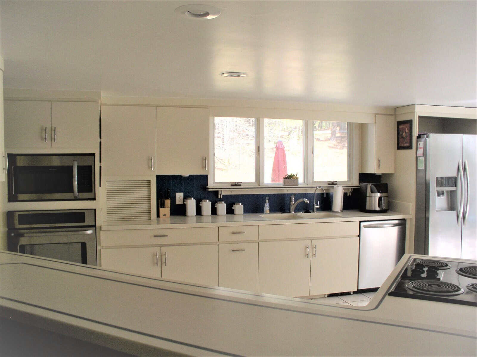 A modern kitchen with white cabinetry, stainless steel appliances, and a blue backsplash, featuring an integrated microwave, a coffee maker, and a stovetop on the counter.