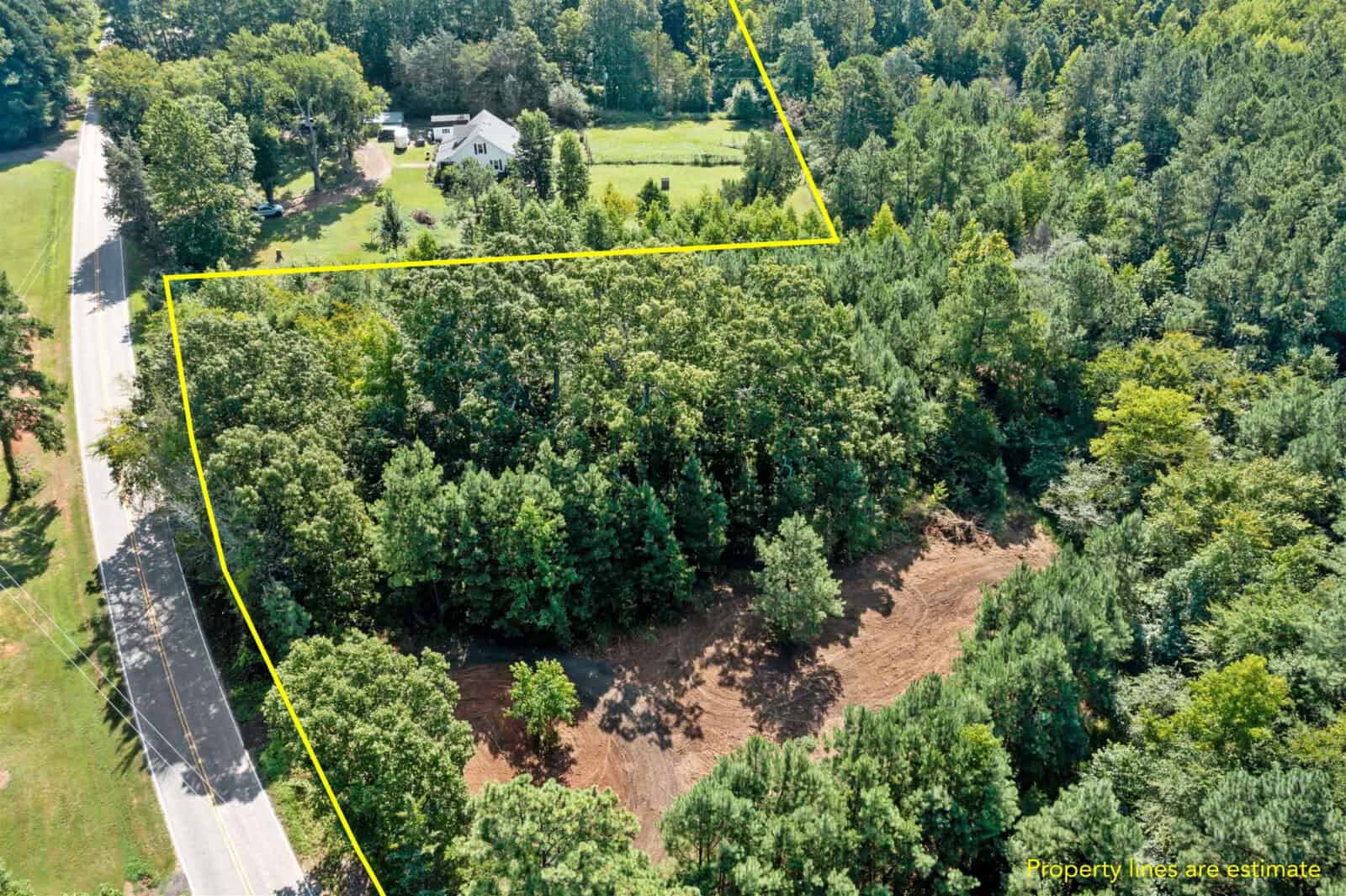 Aerial view of a wooded area outlined in yellow, highlighting the property boundary at 0 Stagecoach Road, Oxford. A cleared section is visible beside a road to the left, with a house and lawn in the upper part of the image. Text reads, "Property lines are estimate.