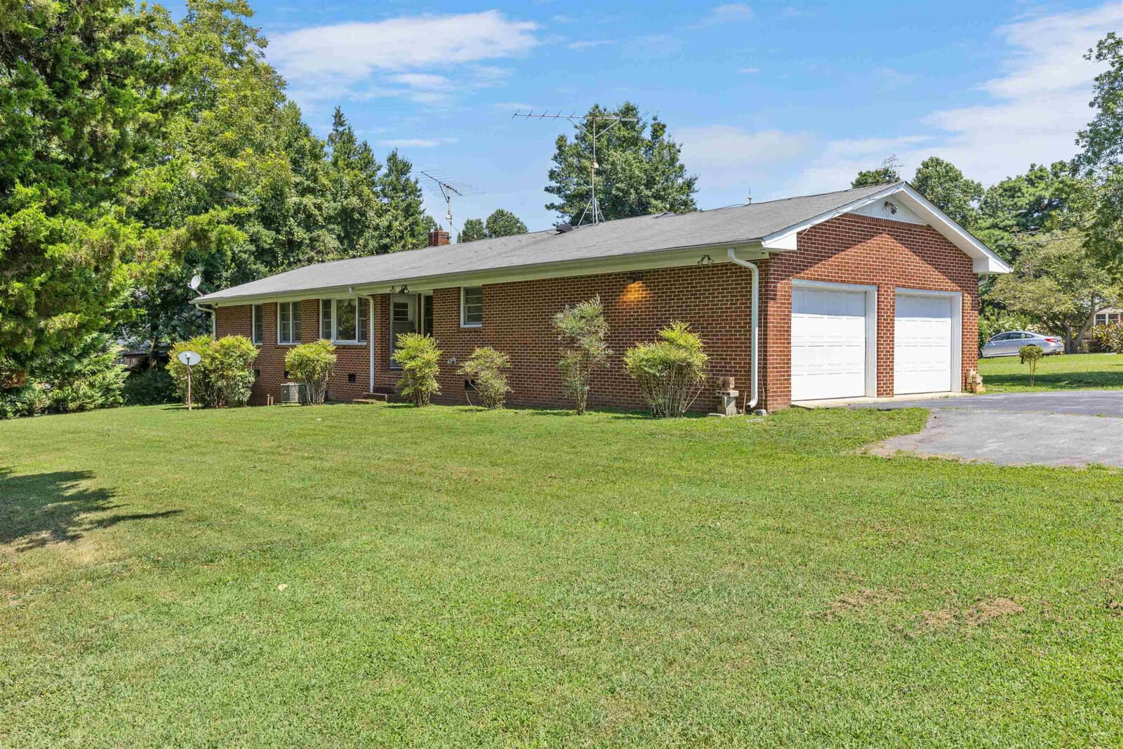 A single-story brick suburban home with a white garage door and driveway on a sunny day with a well-maintained lawn.