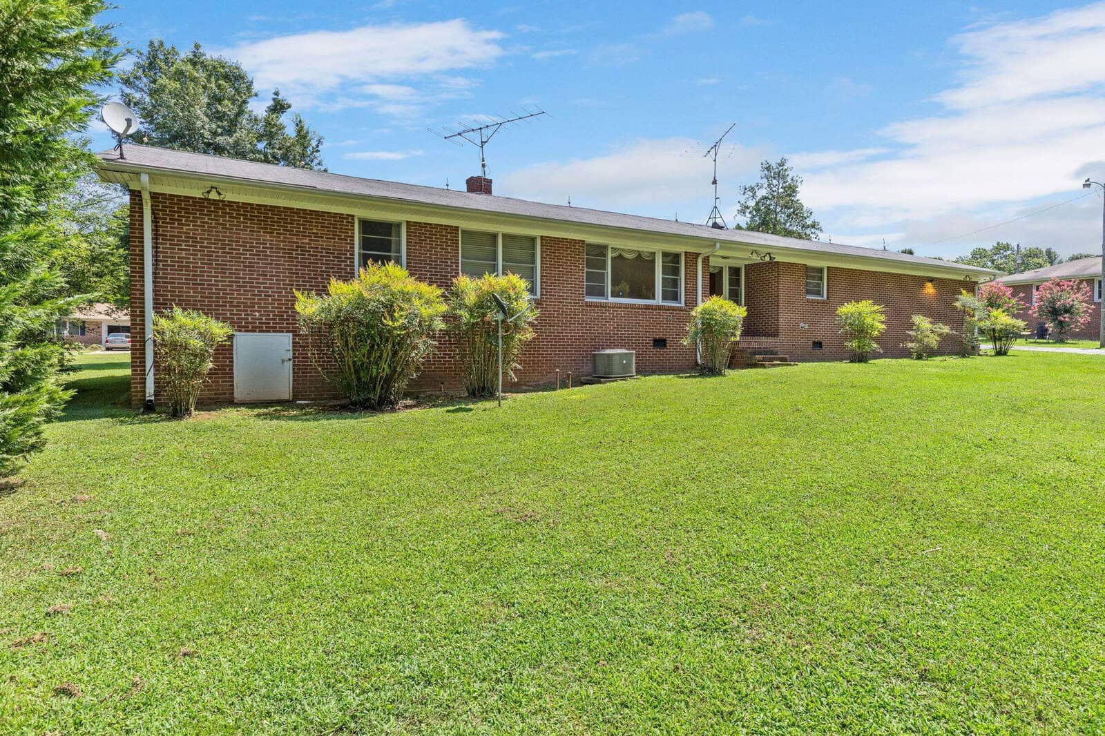 A single-story brick house with a well-kept lawn and shrubbery under a clear blue sky.