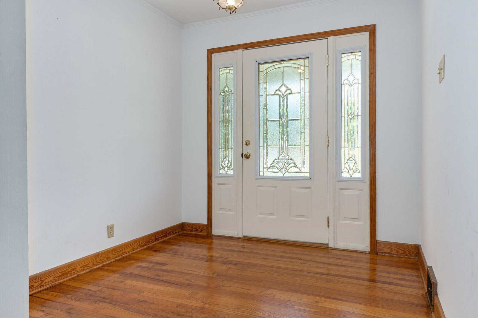 Empty room with white walls, wooden flooring, and a white front door featuring decorative glass panels.