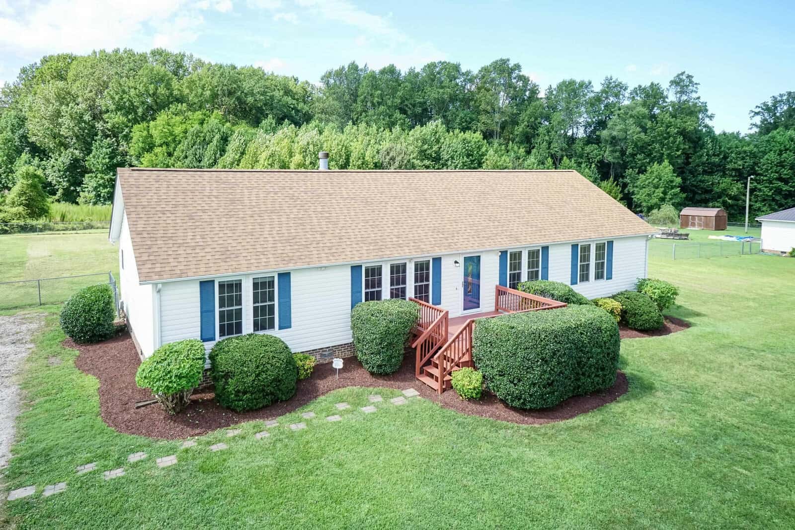 A single-story white house with a gable roof at 575 Stewart Farm Road, Henderson NC, surrounded by manicured bushes and a green lawn, featuring a small wooden deck with stairs at the front