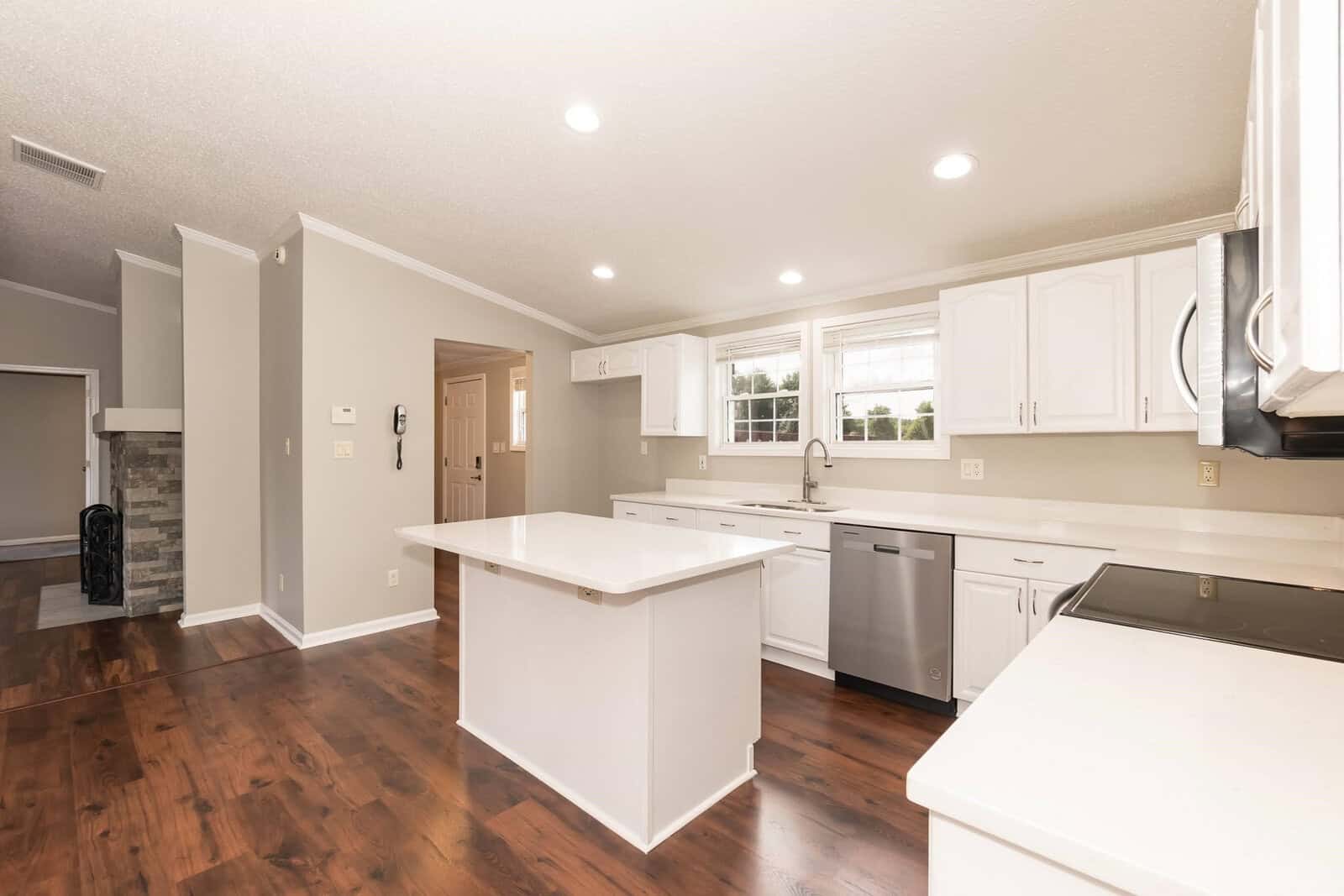 A spacious, well-lit kitchen with modern appliances and hardwood flooring, featuring white cabinetry and a central island.