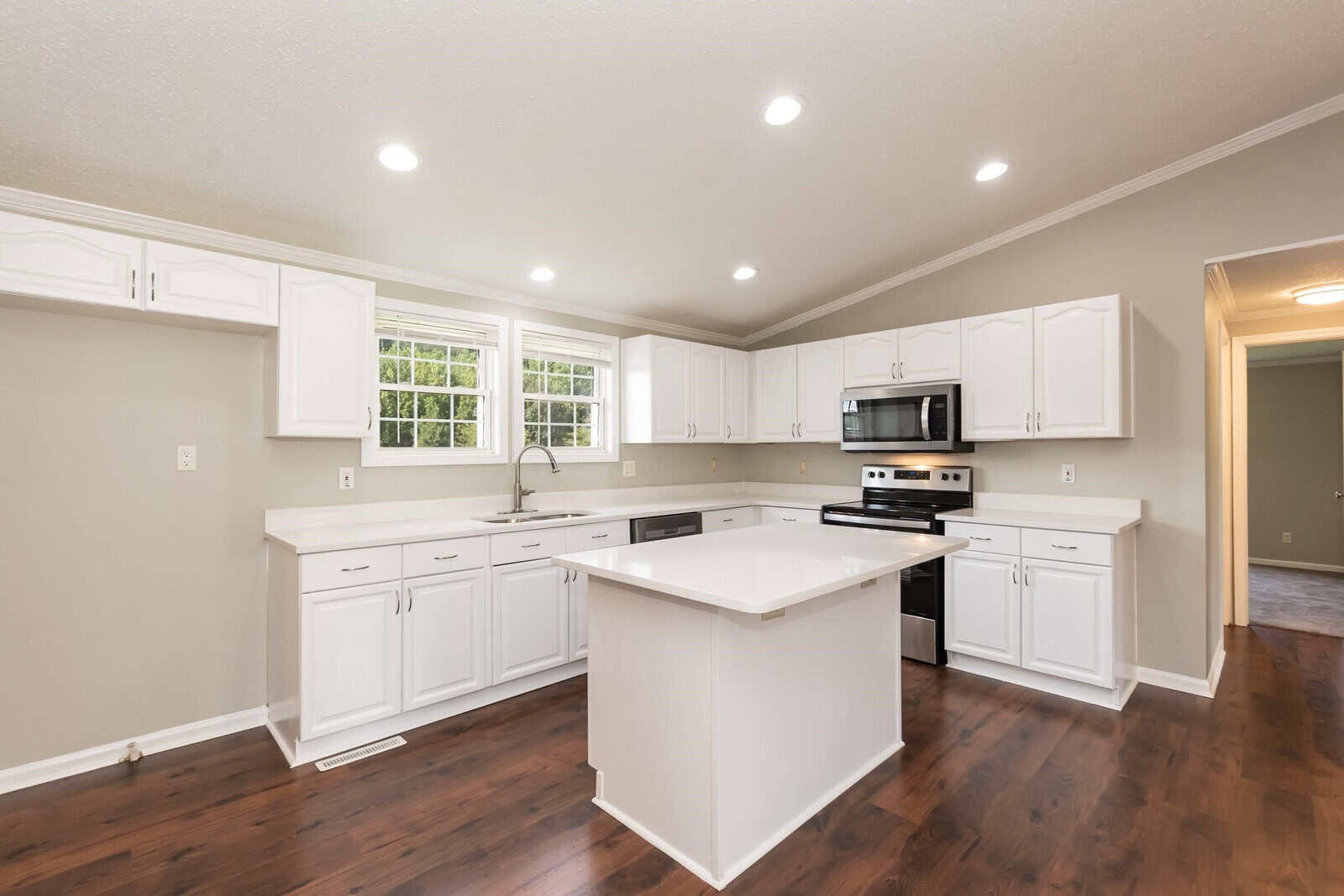 Modern kitchen interior with white cabinets, stainless steel appliances, and a central island in a home with hardwood flooring.