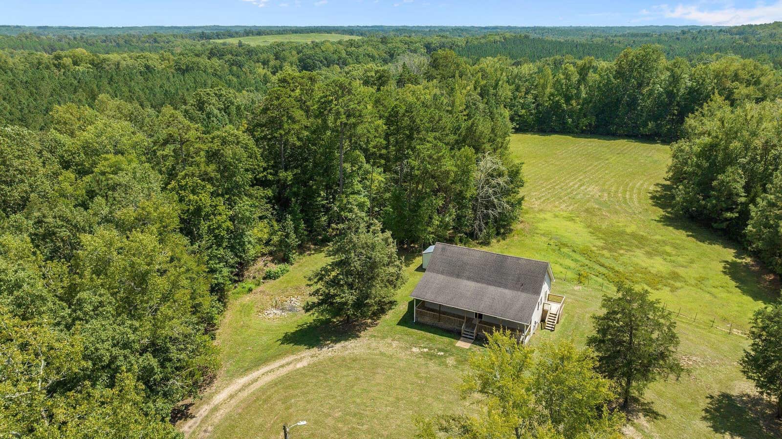Aerial view of a solitary house with a gray roof surrounded by lush greenery and trees with a clear sky above.