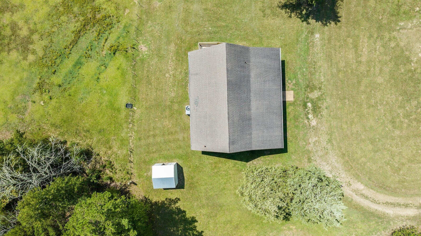 Aerial view of a detached house with a grey roof, surrounded by a green lawn with a small outbuilding and tree nearby.