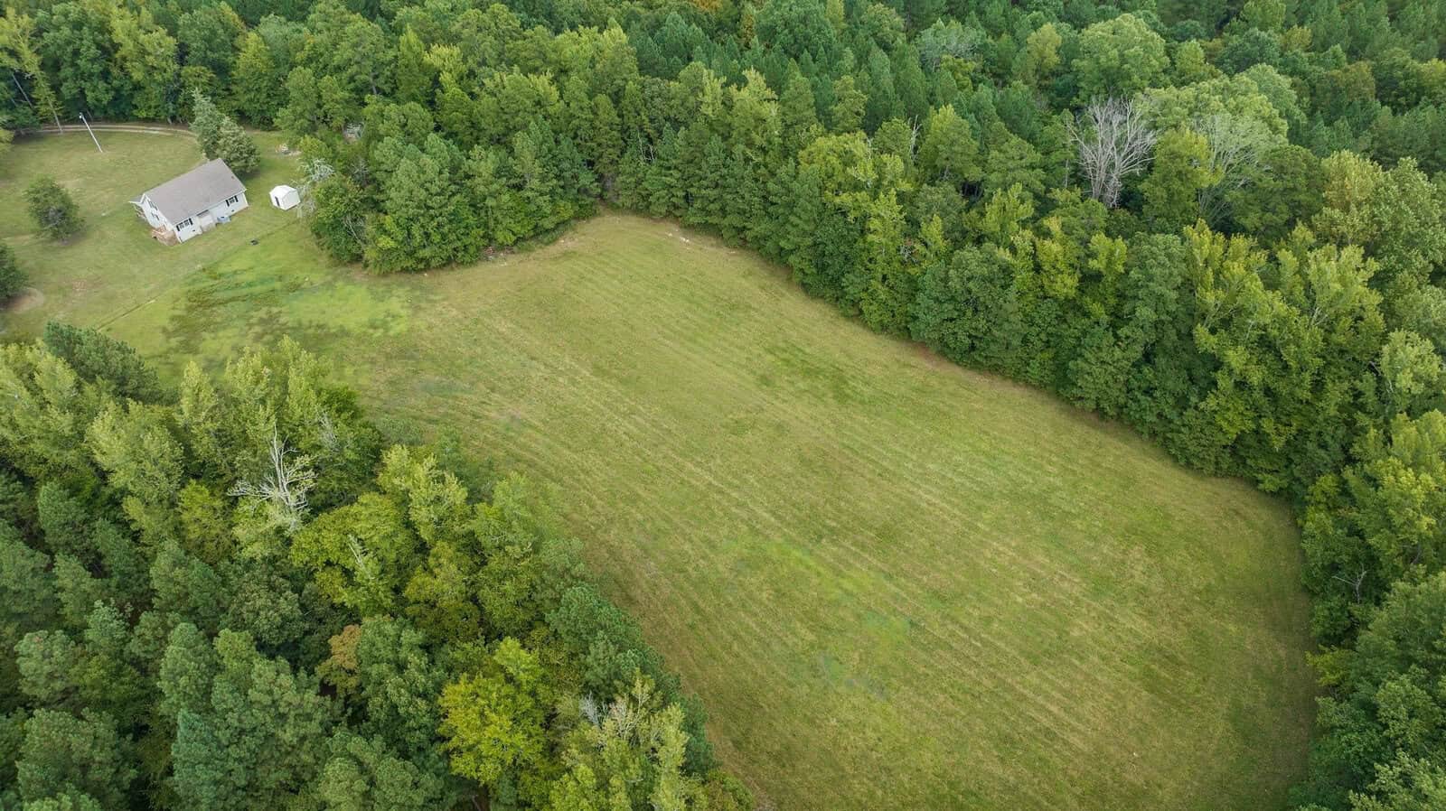 An aerial view of a rural landscape featuring a house with a white exterior surrounded by a vast expanse of green trees and a mowed field.