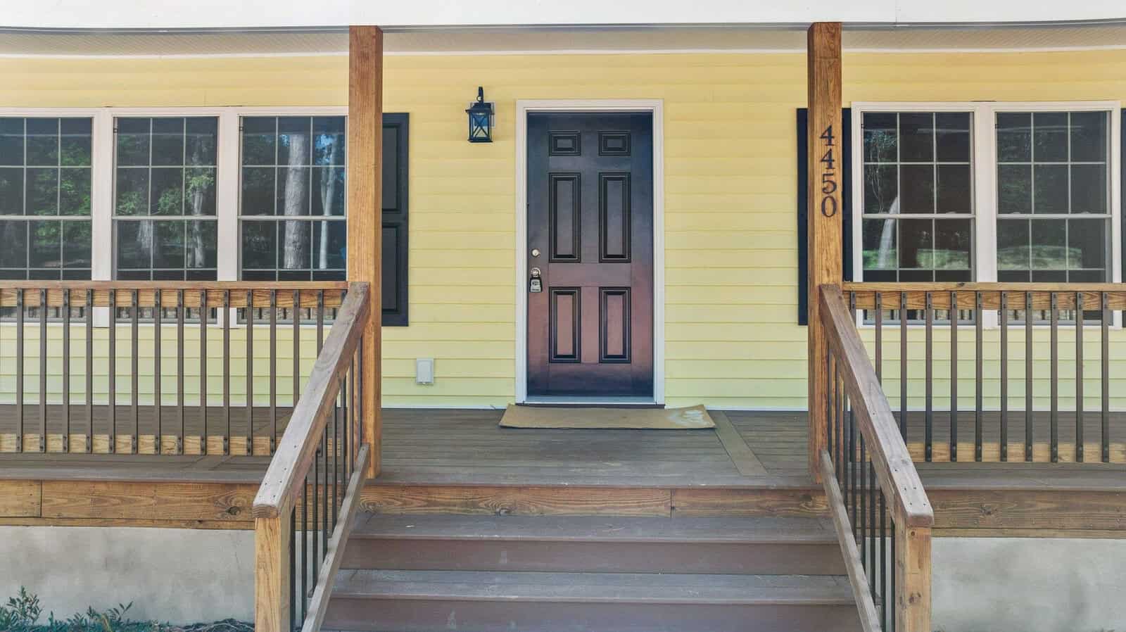 A front porch of a yellow house with a dark-colored door and the house number 4150 displayed above it.