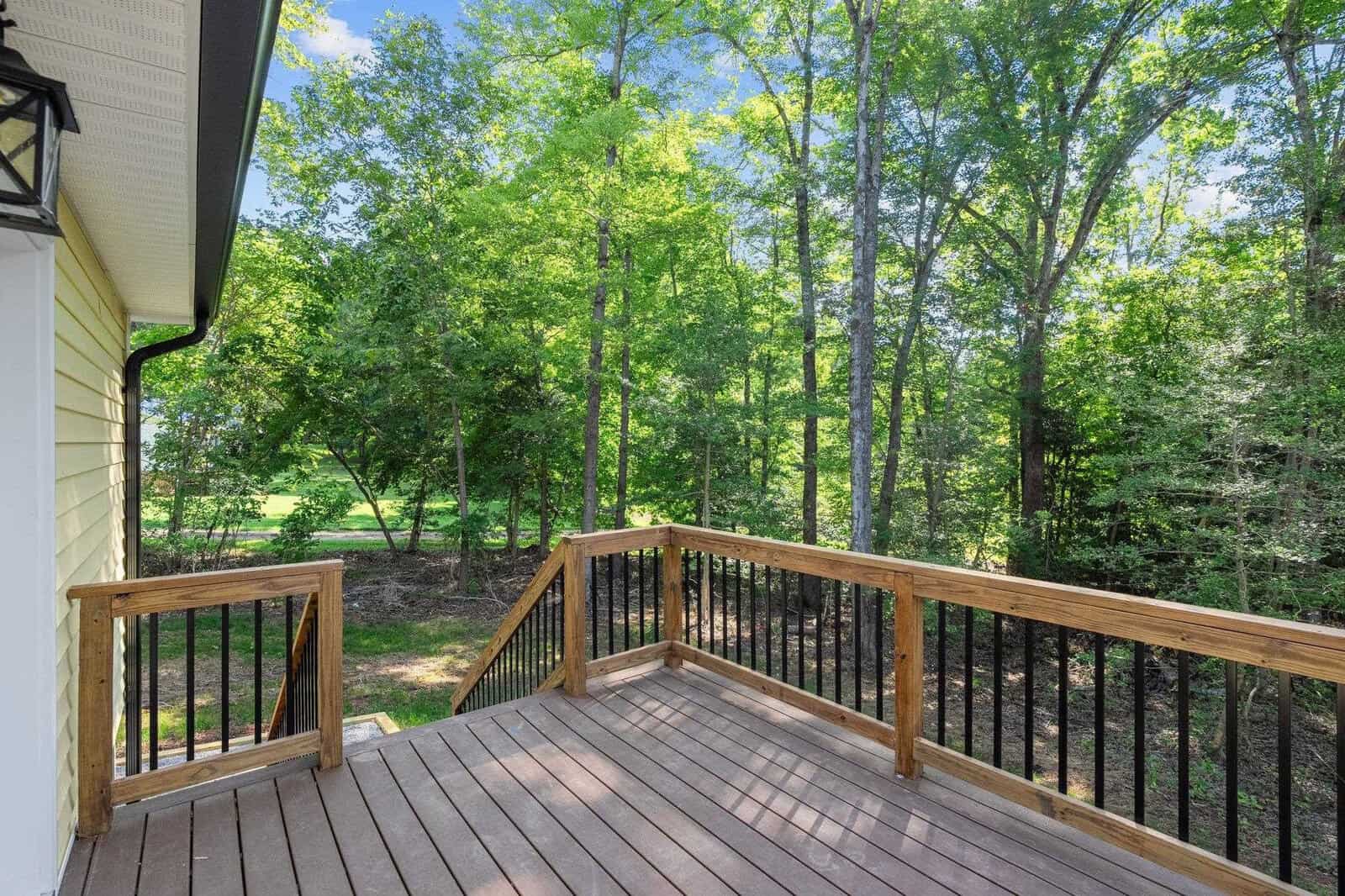 A wooden deck with metal balusters overlooking a verdant backyard with trees.