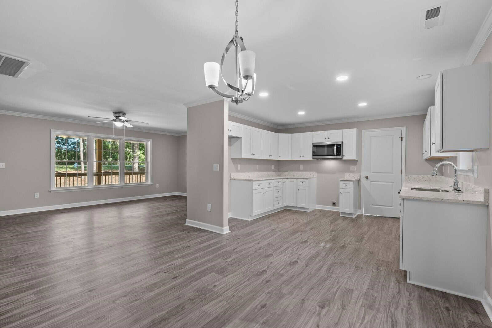 A spacious and modern kitchen with white cabinetry and stainless-steel appliances, opening up to a well-lit living area with wooden flooring and a view of the backyard through sliding glass doors.