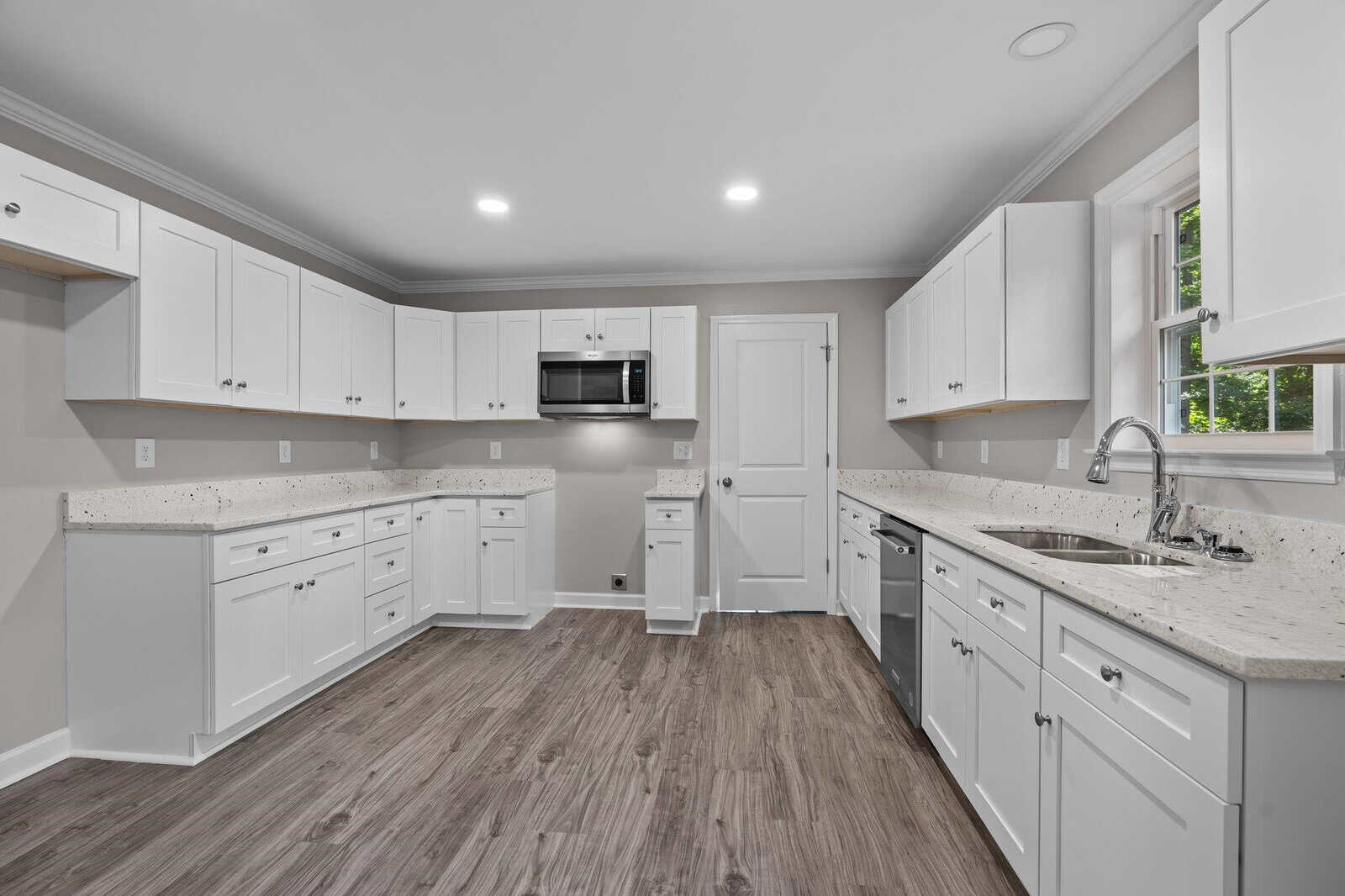 A modern kitchen with white cabinetry, stainless steel appliances, granite countertops, and laminate wood flooring.