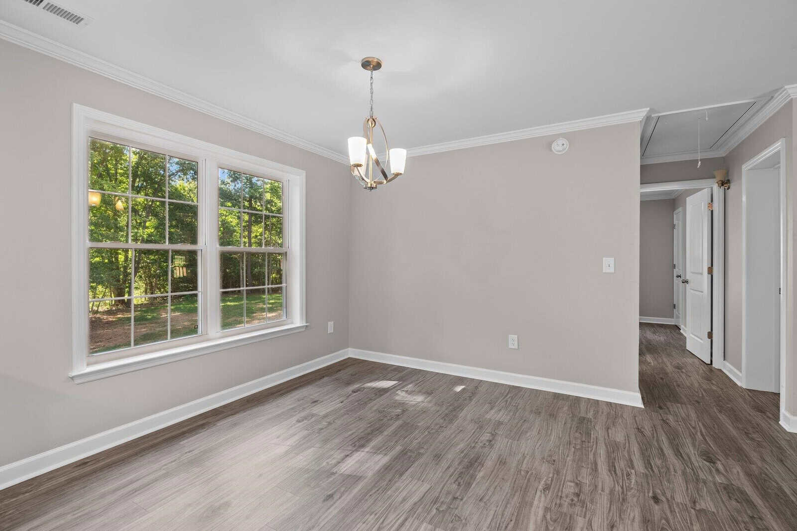 Empty room with gray walls, laminate flooring, and a window overlooking trees.