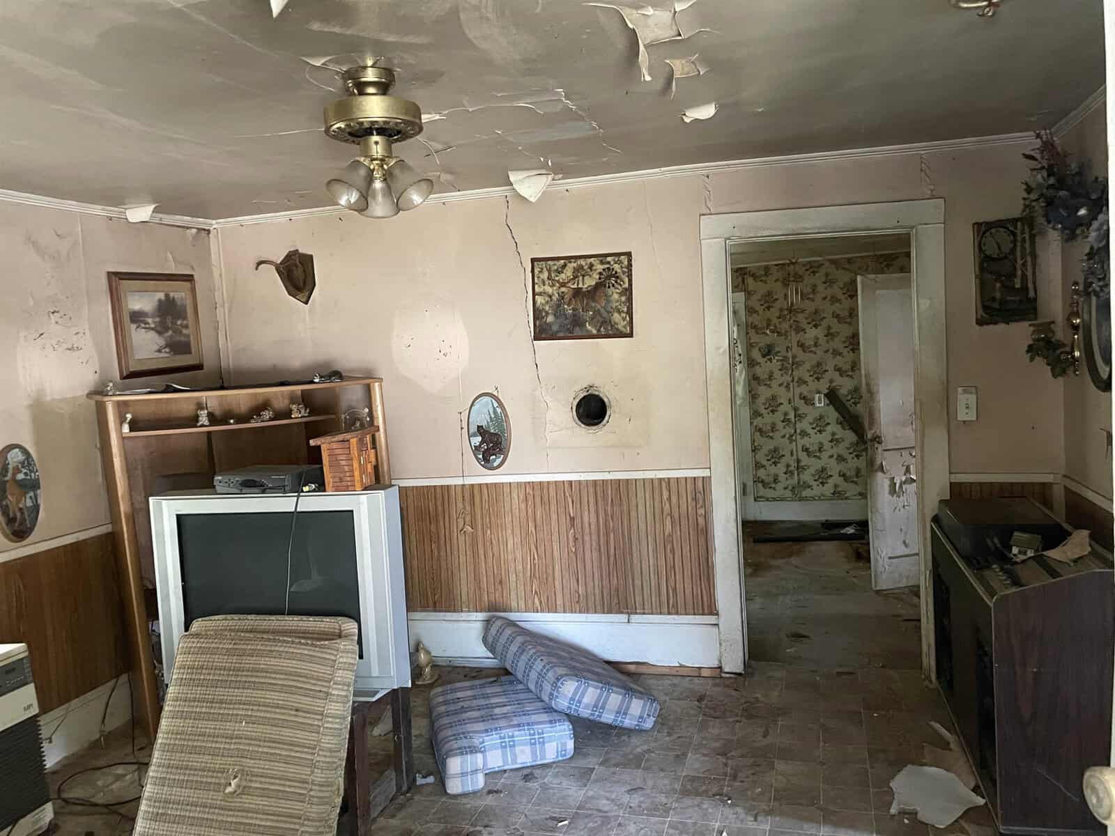A dilapidated room with peeling paint, a fallen ceiling, old furniture, and debris scattered on the floor.